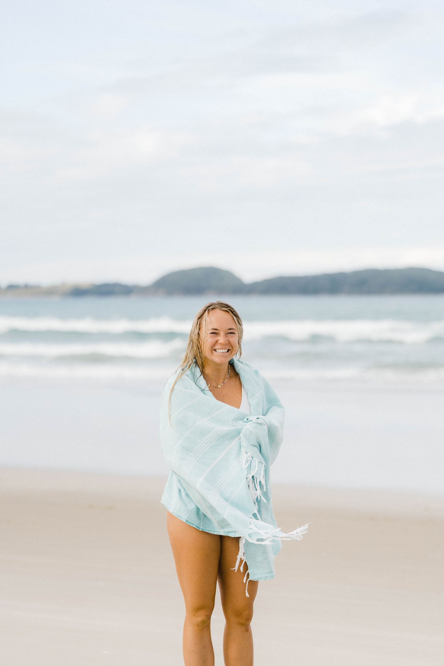 Person wrapped in light blue cover enjoying a peaceful moment on a sandy beach.
