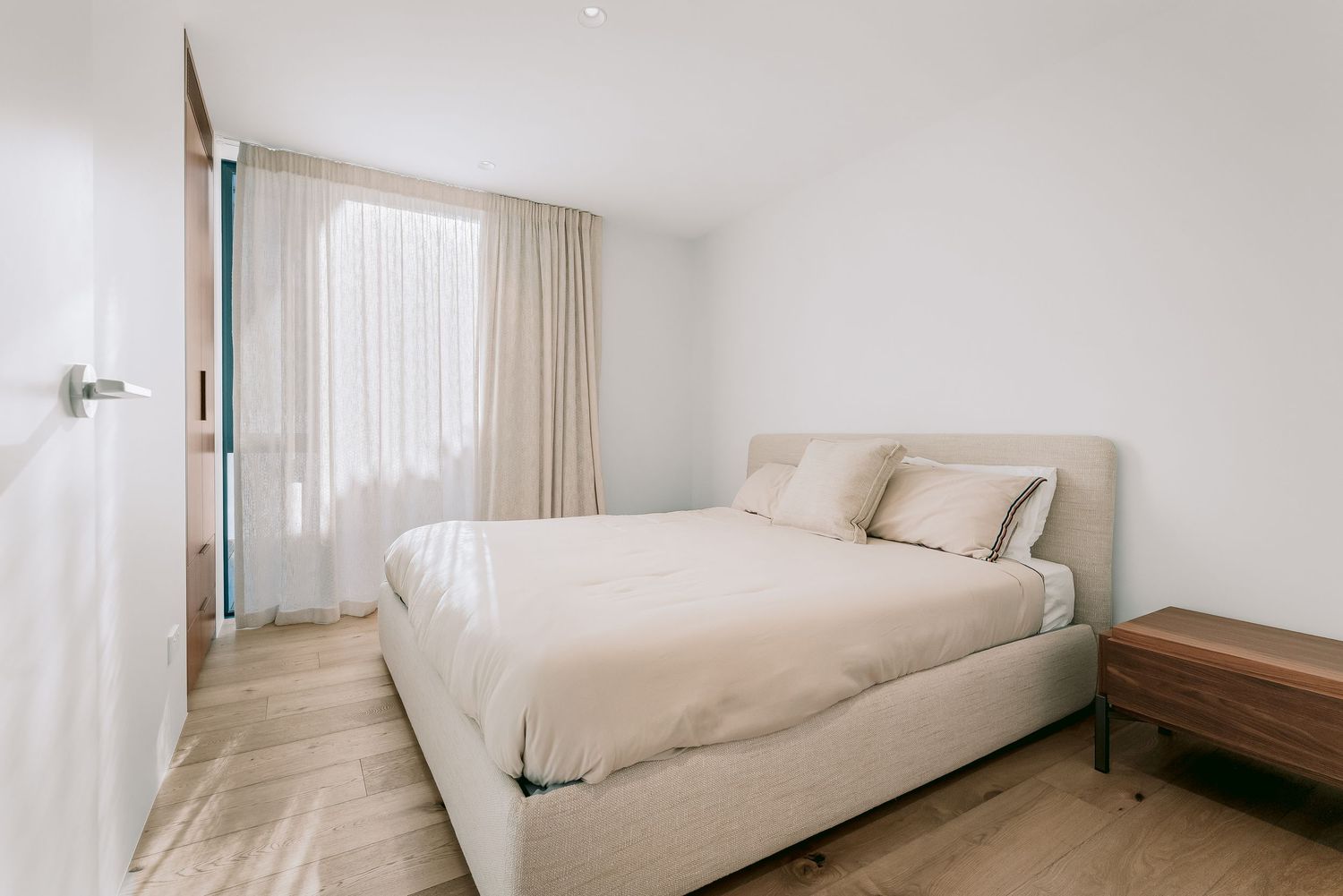 Minimalist bedroom interior with white bedding and natural light flowing through windows.