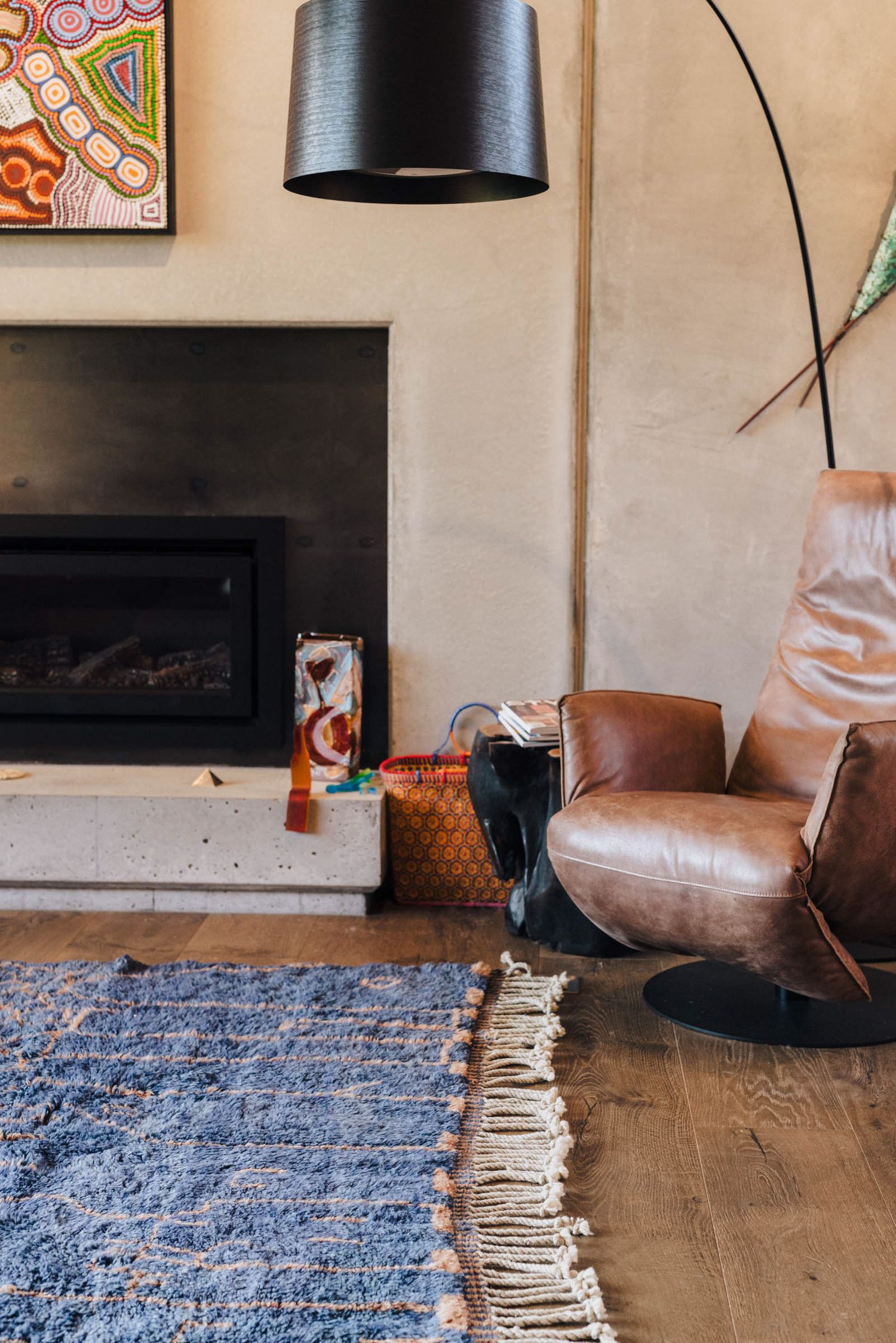 Cozy living room interior with leather chair, blue rug, black floor lamp and modern fireplace setup.