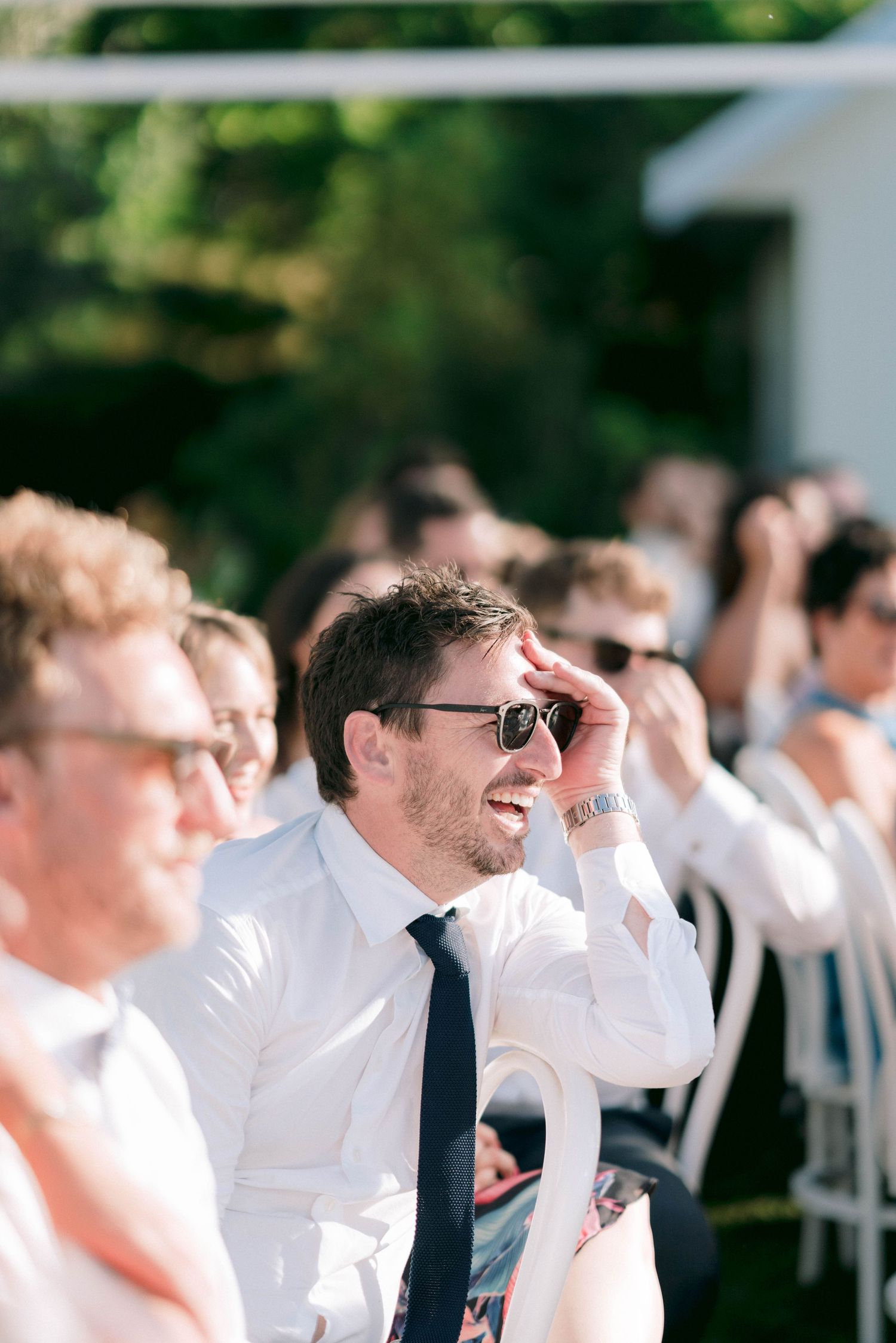 Wedding guests in white shirts and ties laughing together during an outdoor celebration.