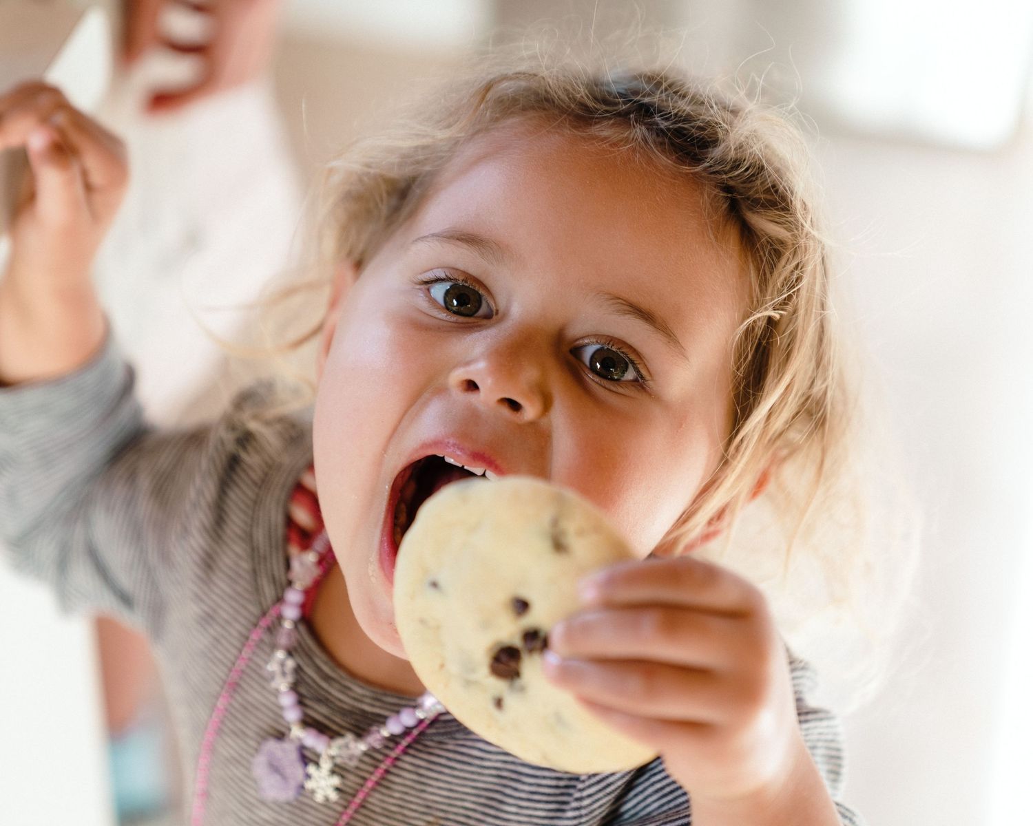 Child enjoying a cookie or biscuit with visible chocolate chips or fruit pieces.