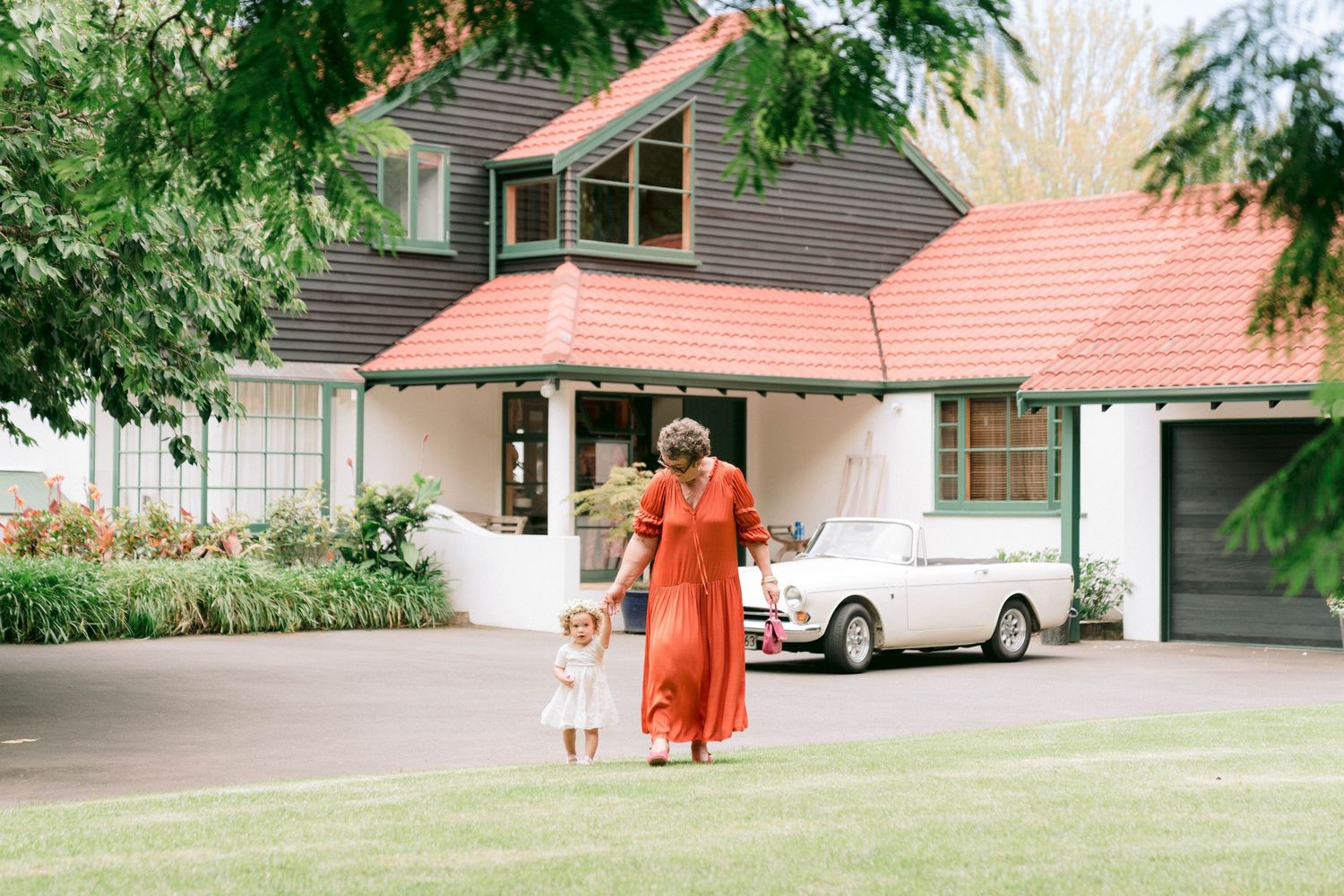 A vintage orange Volkswagen Beetle parked in front of a suburban house with a terracotta roof.