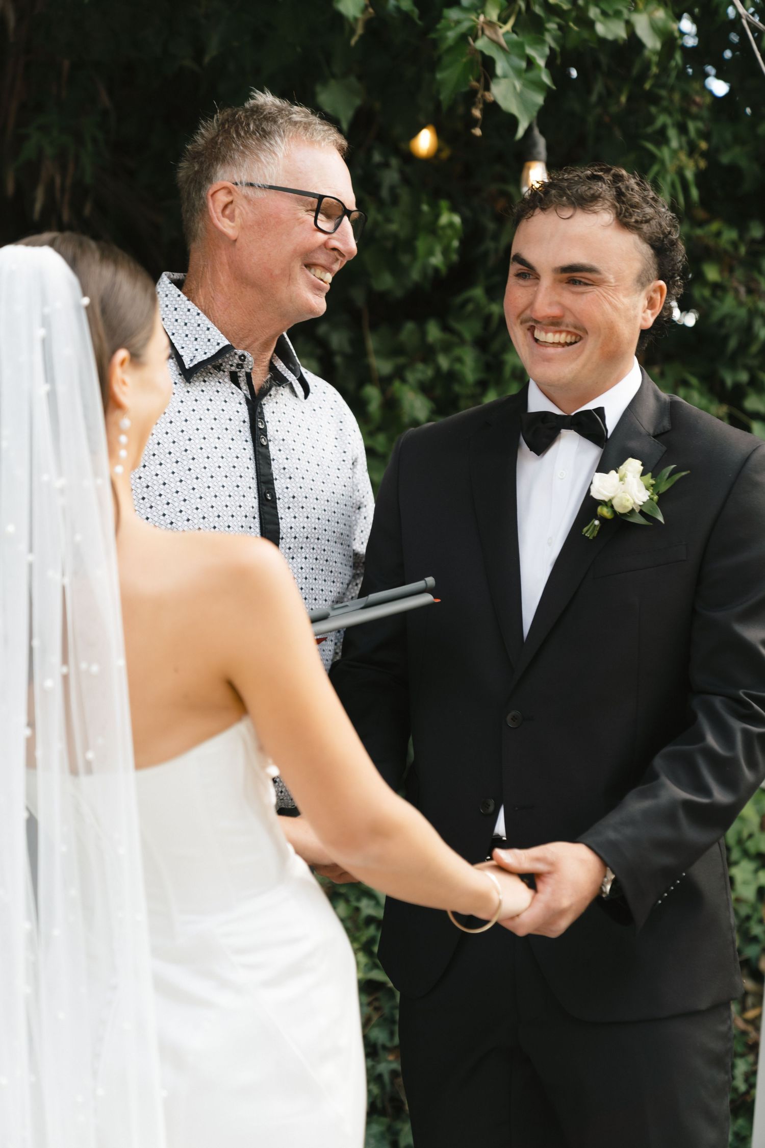 Wedding ceremony with officiant and couple exchanging vows under greenery.