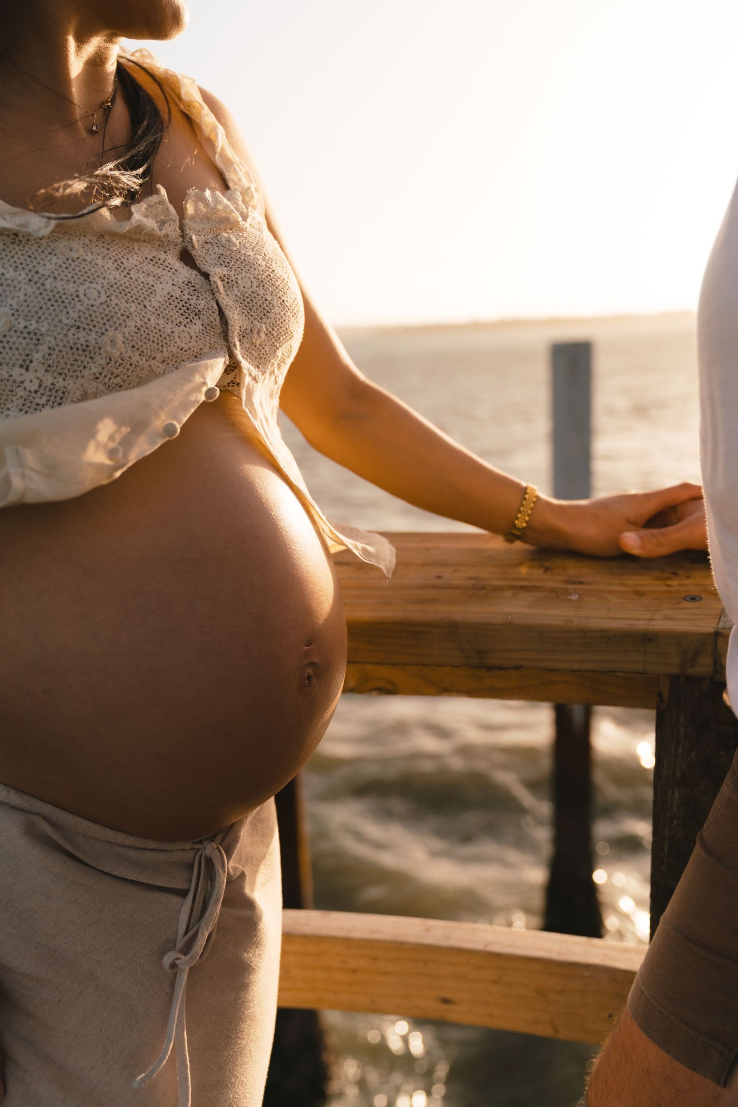 Close-up view of pregnant belly basking in golden sunlight on wooden deck.