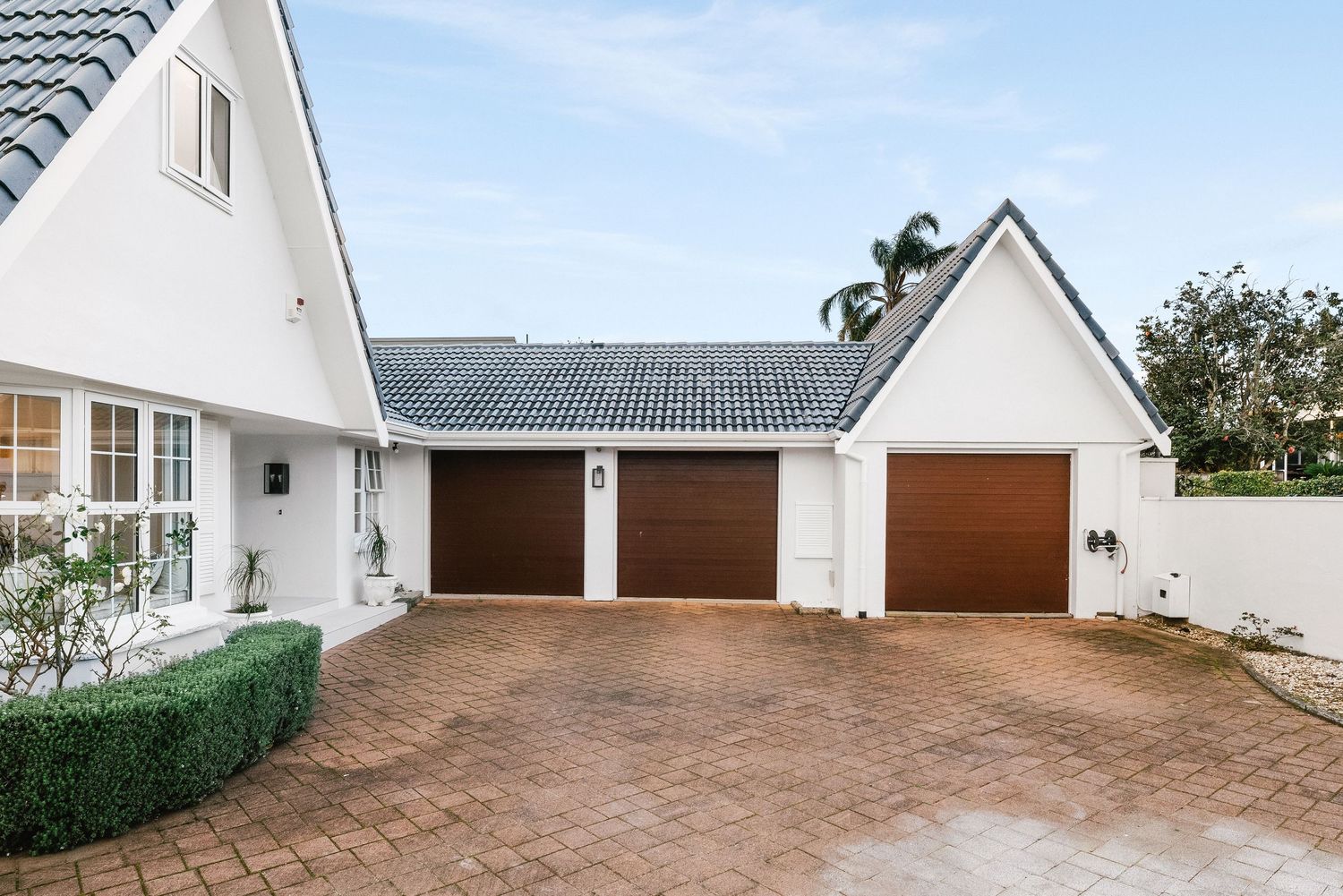White A-frame house exterior with three-car garage and brick driveway.