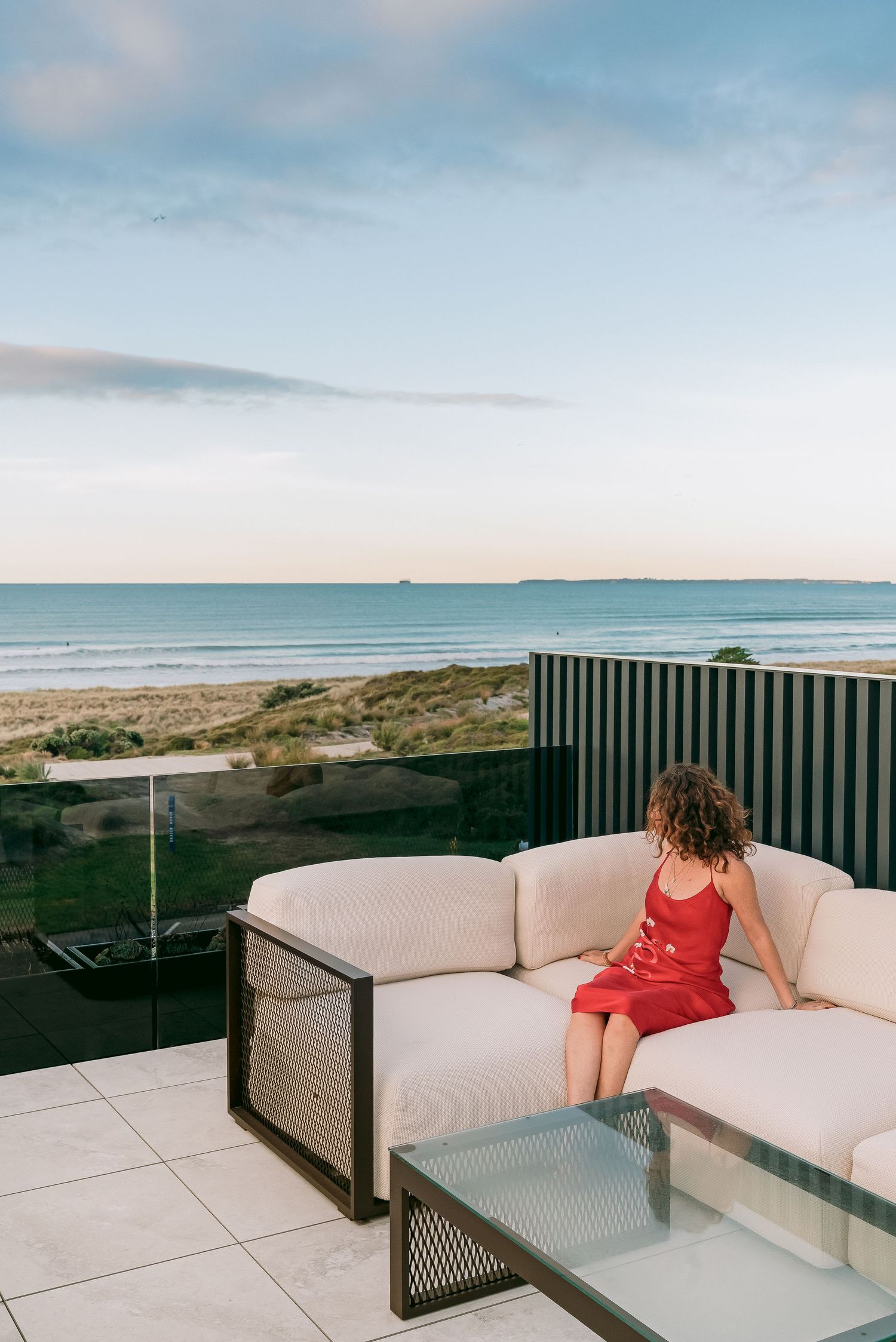 Ocean view from a modern rooftop terrace featuring white outdoor seating and glass safety barriers.