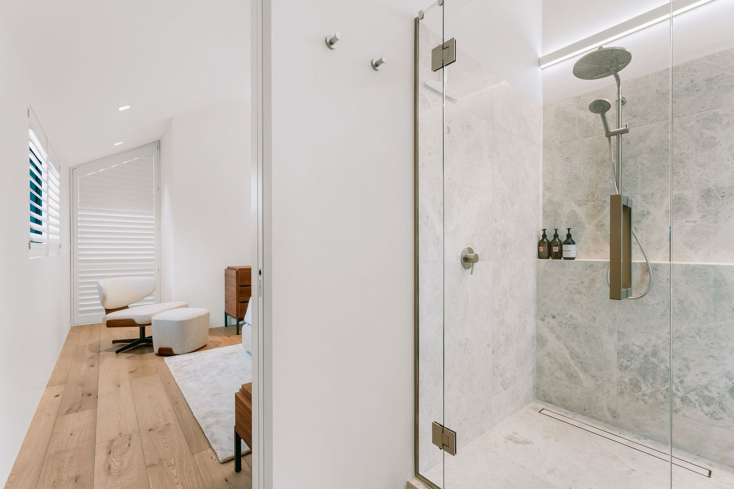 Light-filled bathroom hallway with wooden floors, white walls, and glass shower enclosure.