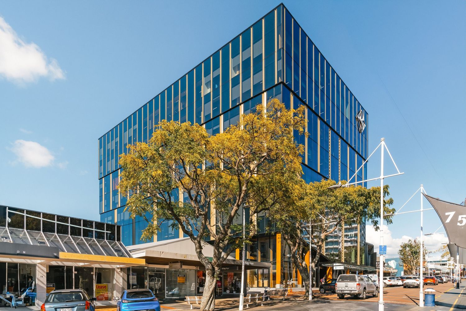 Modern office building with blue glass exterior and autumn trees in front of the entrance.