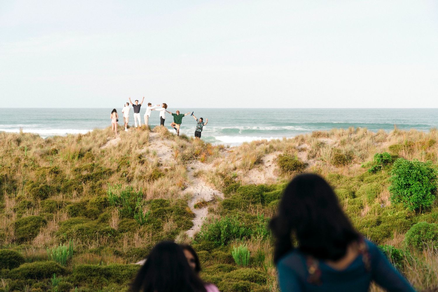 People walking along a grassy coastal path overlooking the ocean.