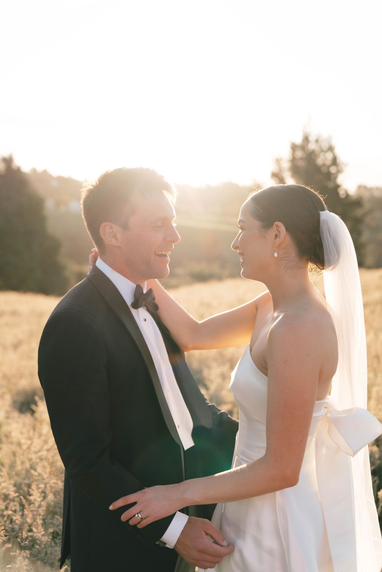 Tender moment between newlyweds in formal attire during golden hour sunset.