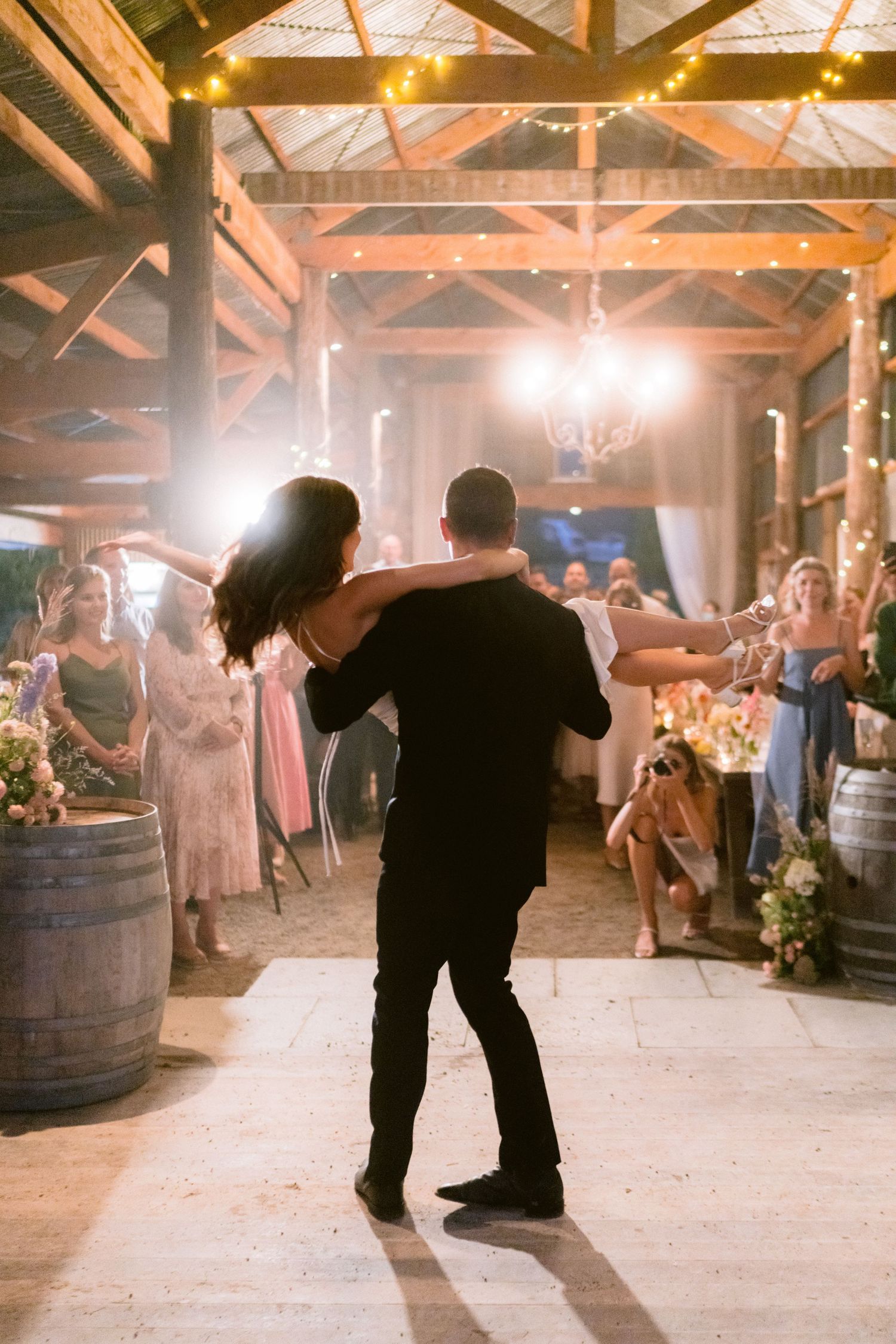 Silhouetted couples dance on a rustic wooden floor under warm barn lighting.