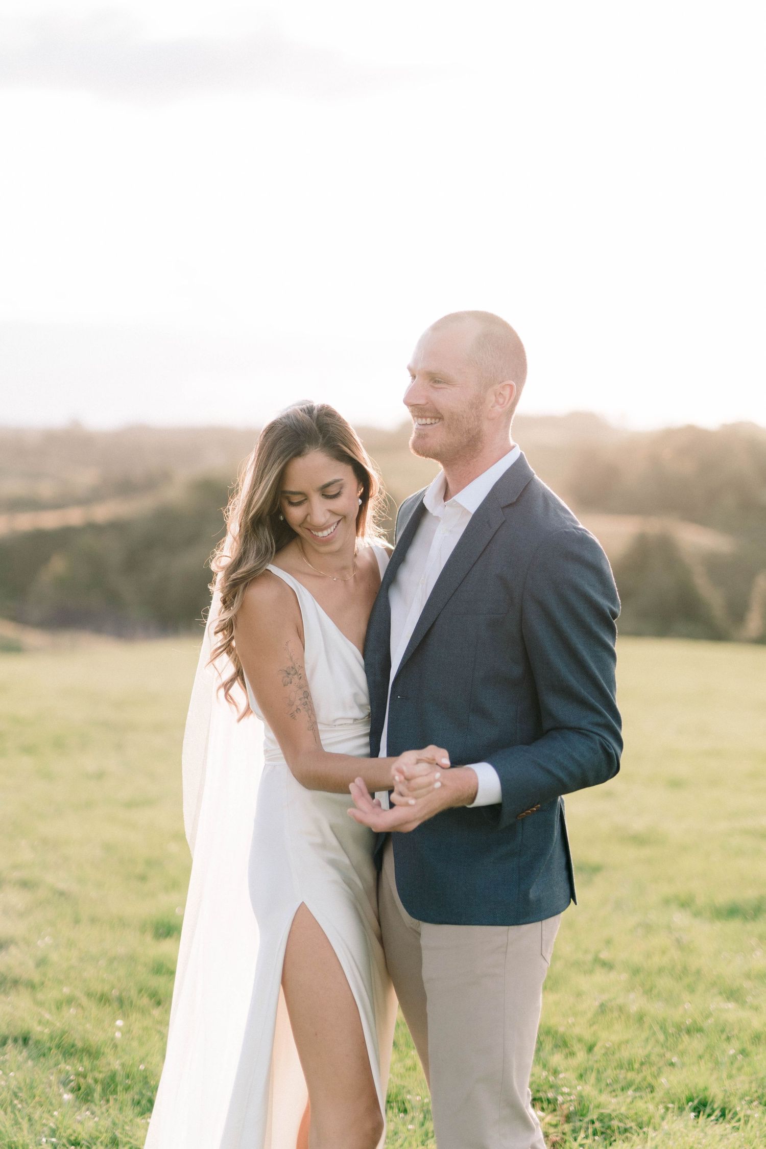Couple embraces in an elegant outdoor photoshoot against a rolling hills landscape at sunset.
