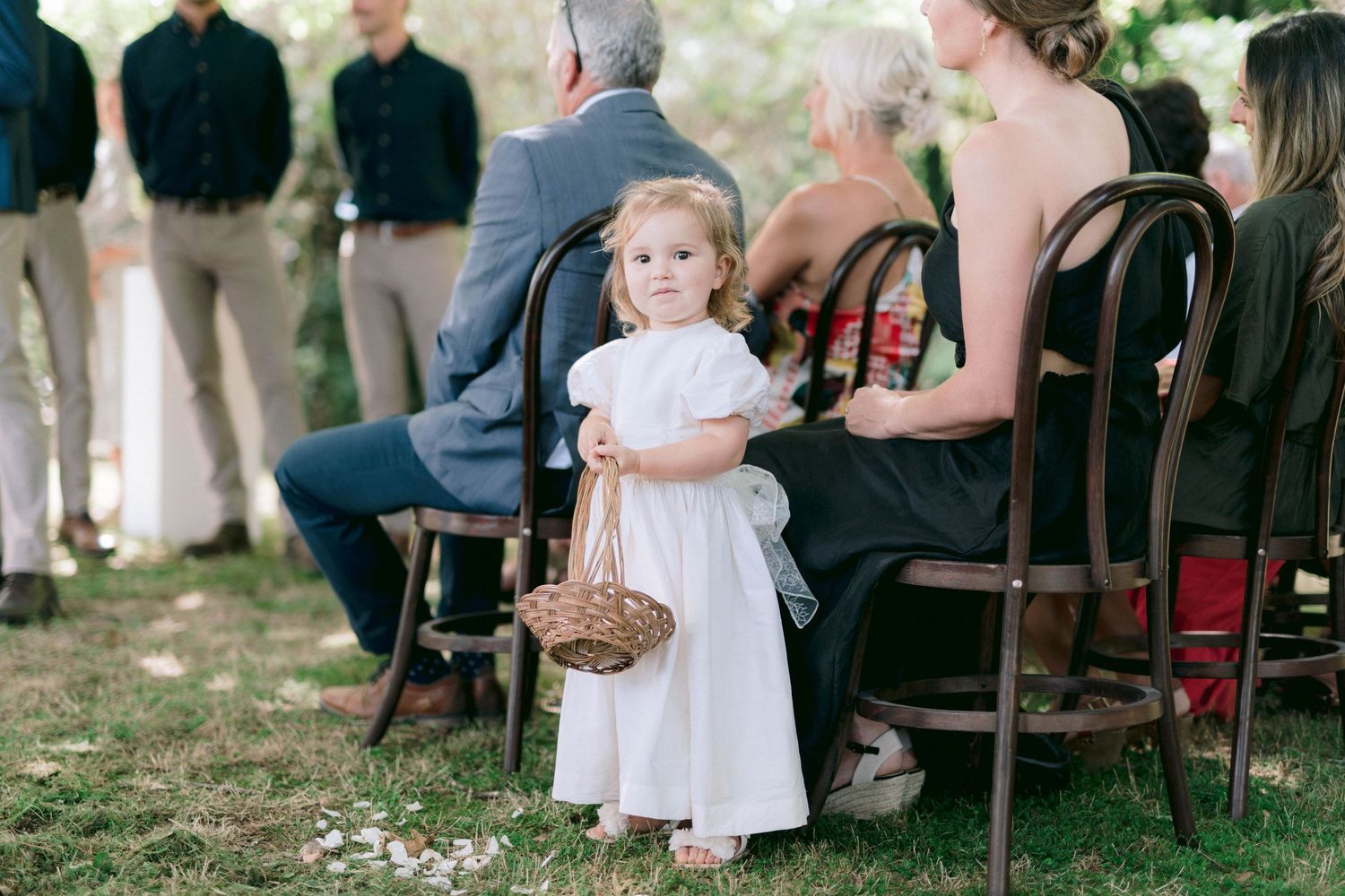 Wedding ceremony seating arrangement with wooden chairs on grass under tall trees.