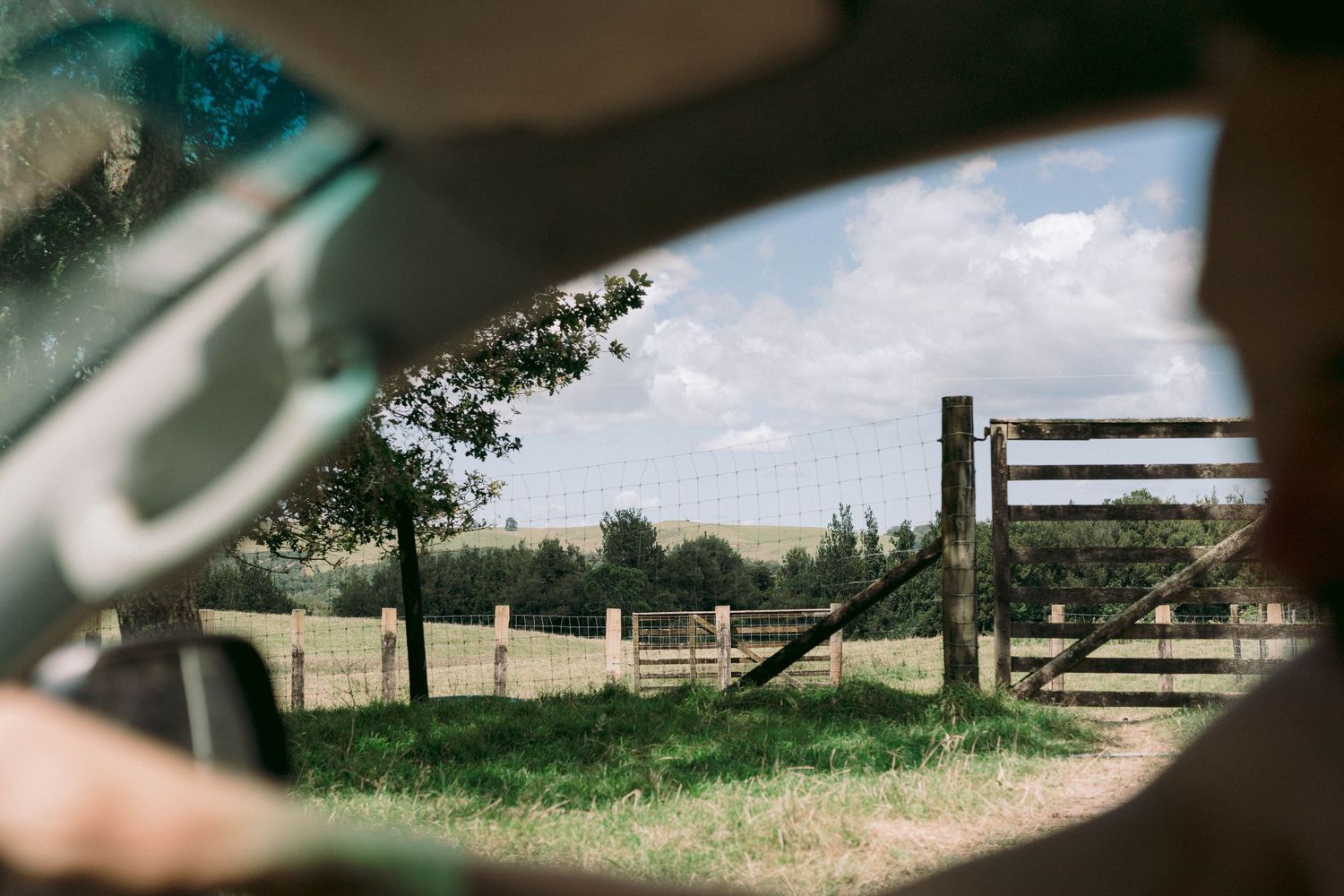 Scenic rural landscape view through a car window showing green fields and wooden fences.