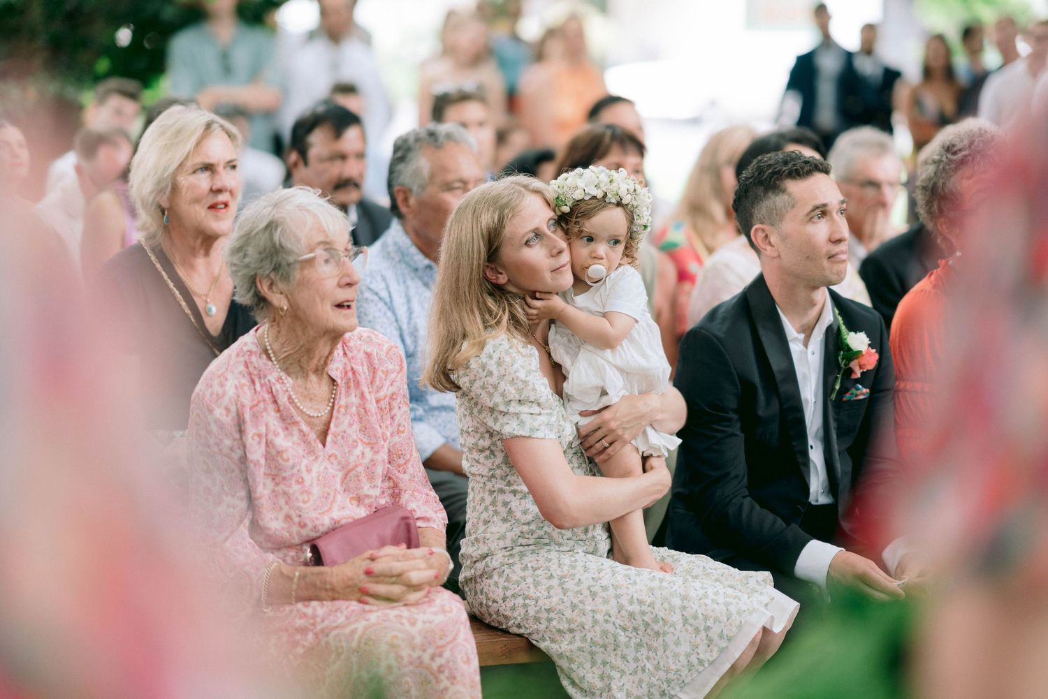 Wedding guests seated outdoors watching ceremony with joyful expressions.