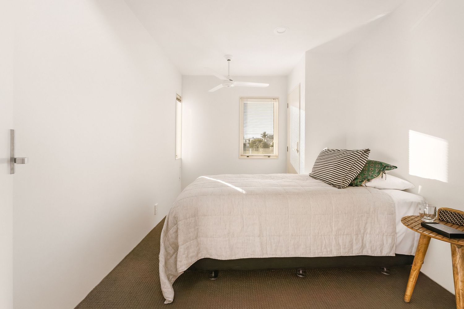 Bright white bedroom interior with minimal decor and natural light streaming through windows.