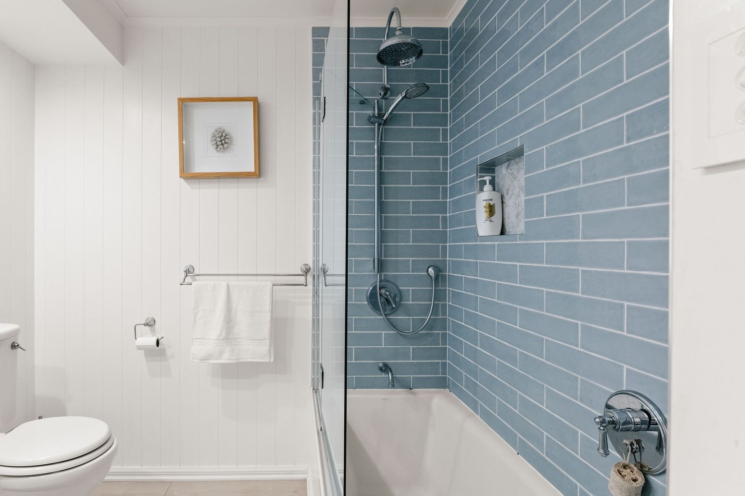 Modern bathroom featuring blue subway tile walls, glass shower enclosure, and clean white fixtures.