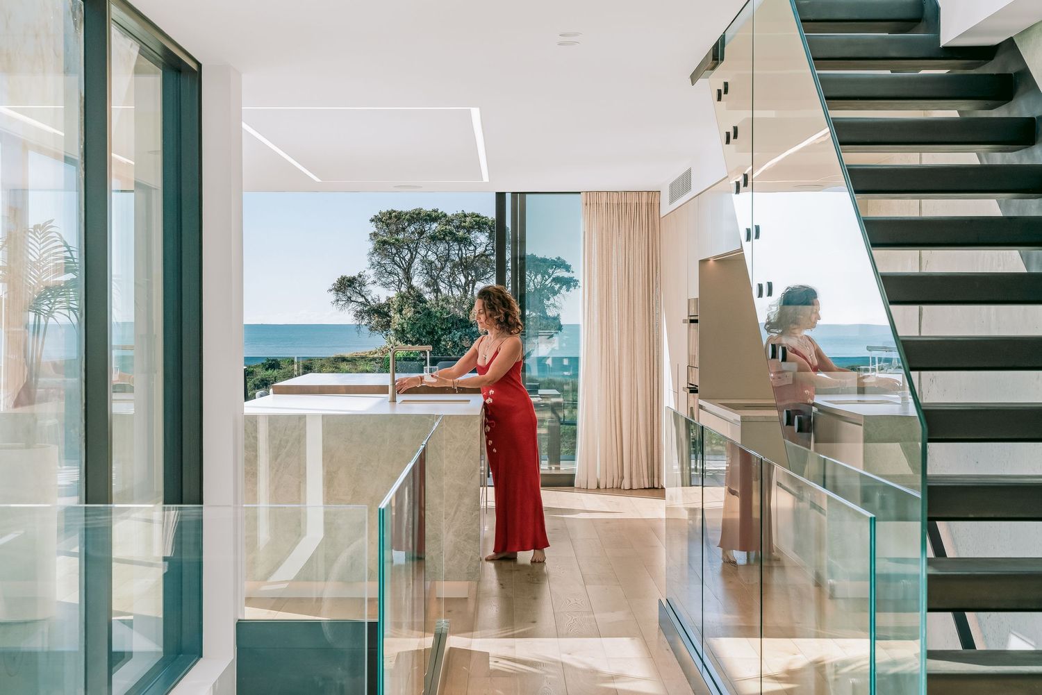 Modern luxury home interior with sleek floating staircase and floor-to-ceiling windows overlooking ocean views.