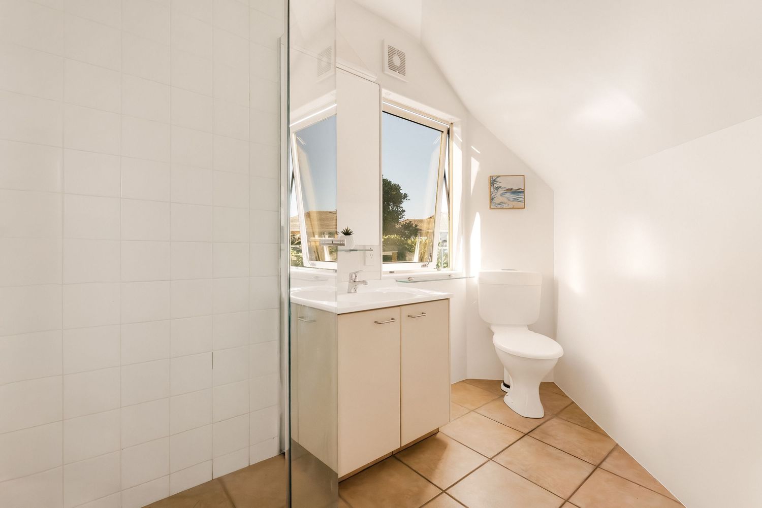Clean modern bathroom with glass shower, white vanity and tiled flooring.
