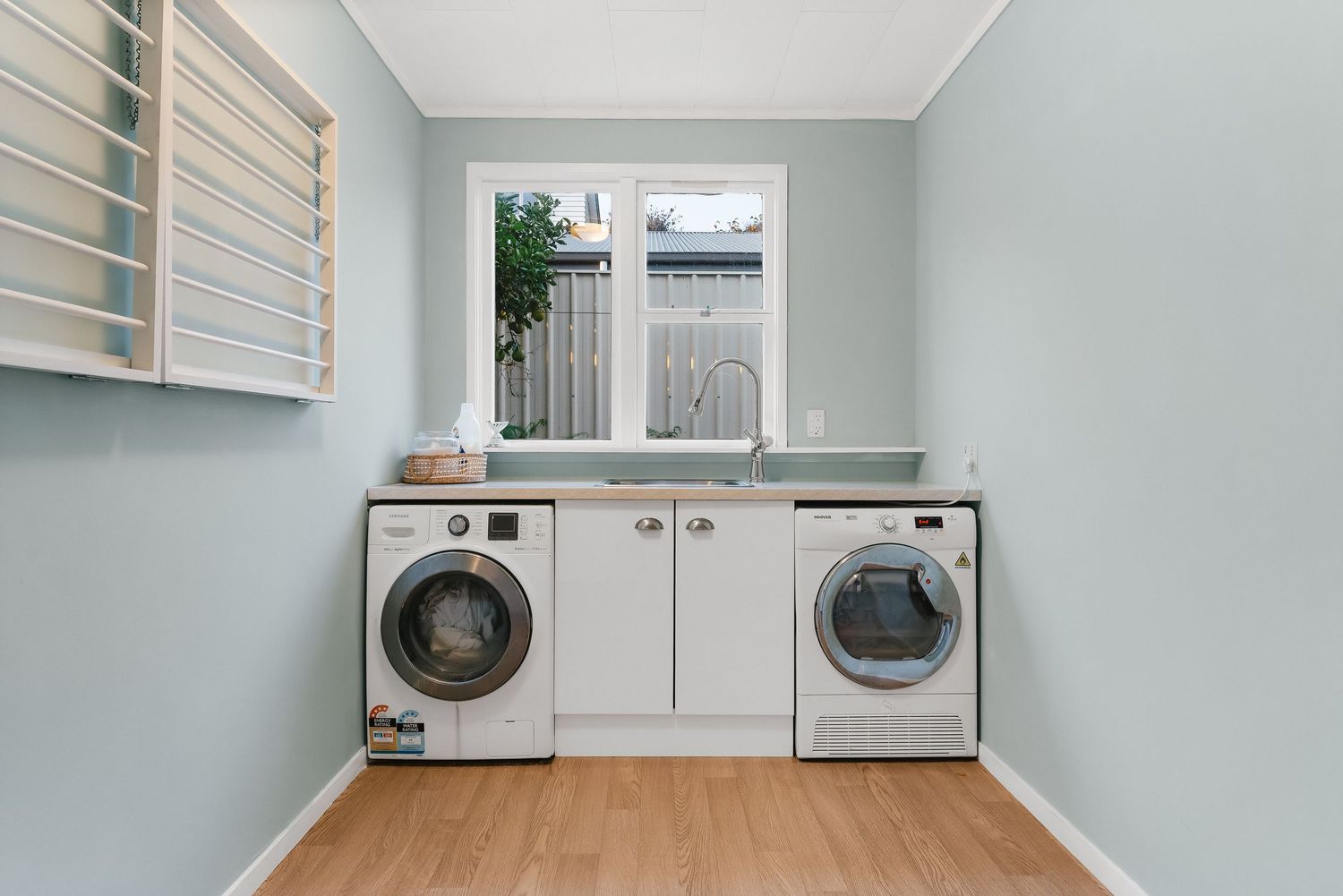 Modern laundry room with two white washers and wooden flooring.