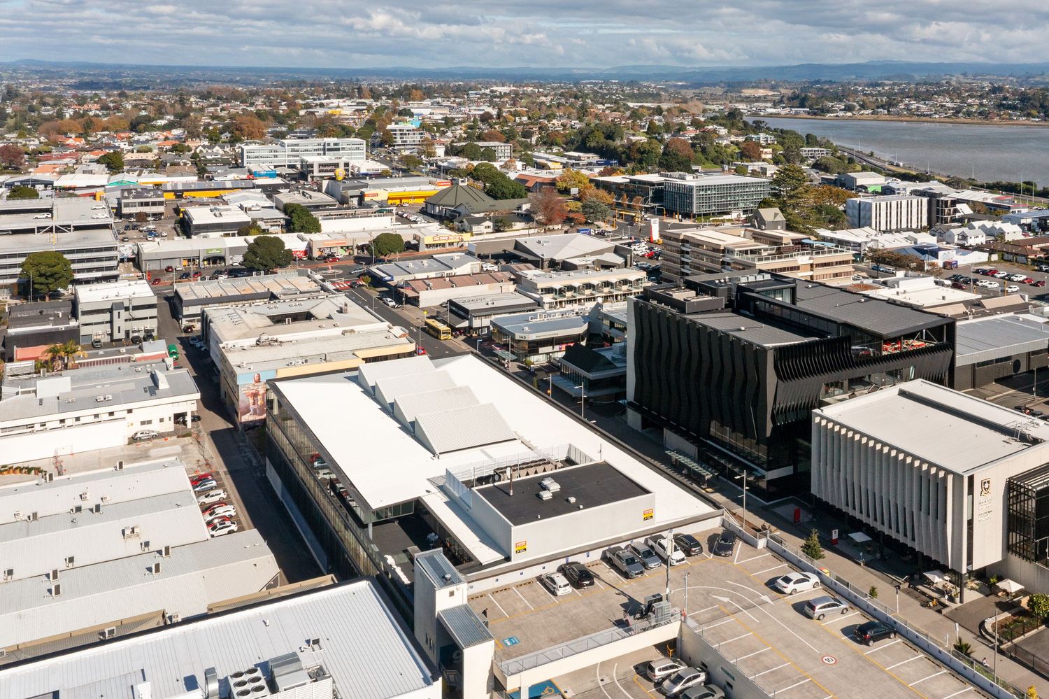 Aerial panorama of an urban cityscape showing commercial buildings and parking lots with mountains in the distance.