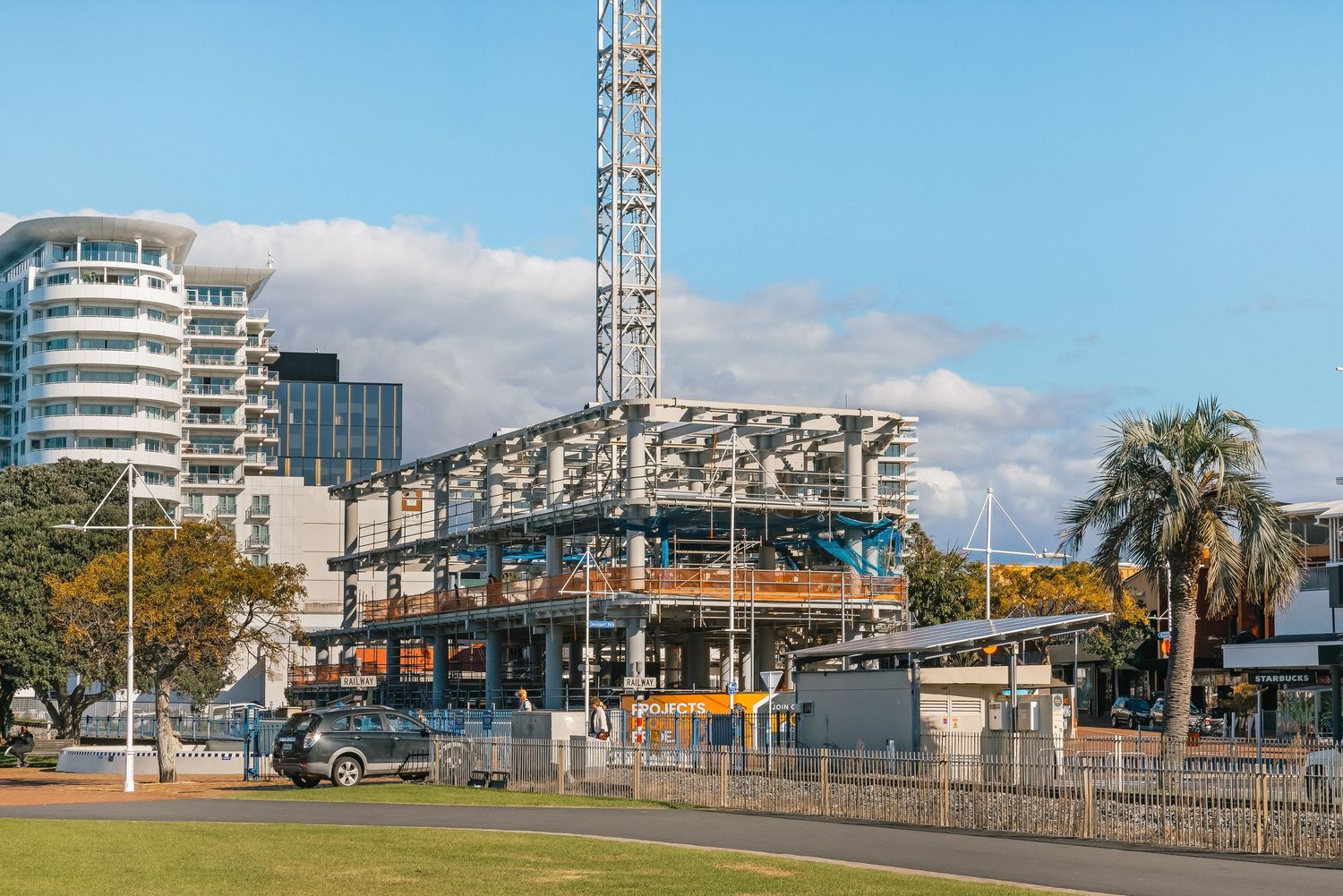 Construction site with a tower crane and modern building development against blue sky with palm trees in urban setting.