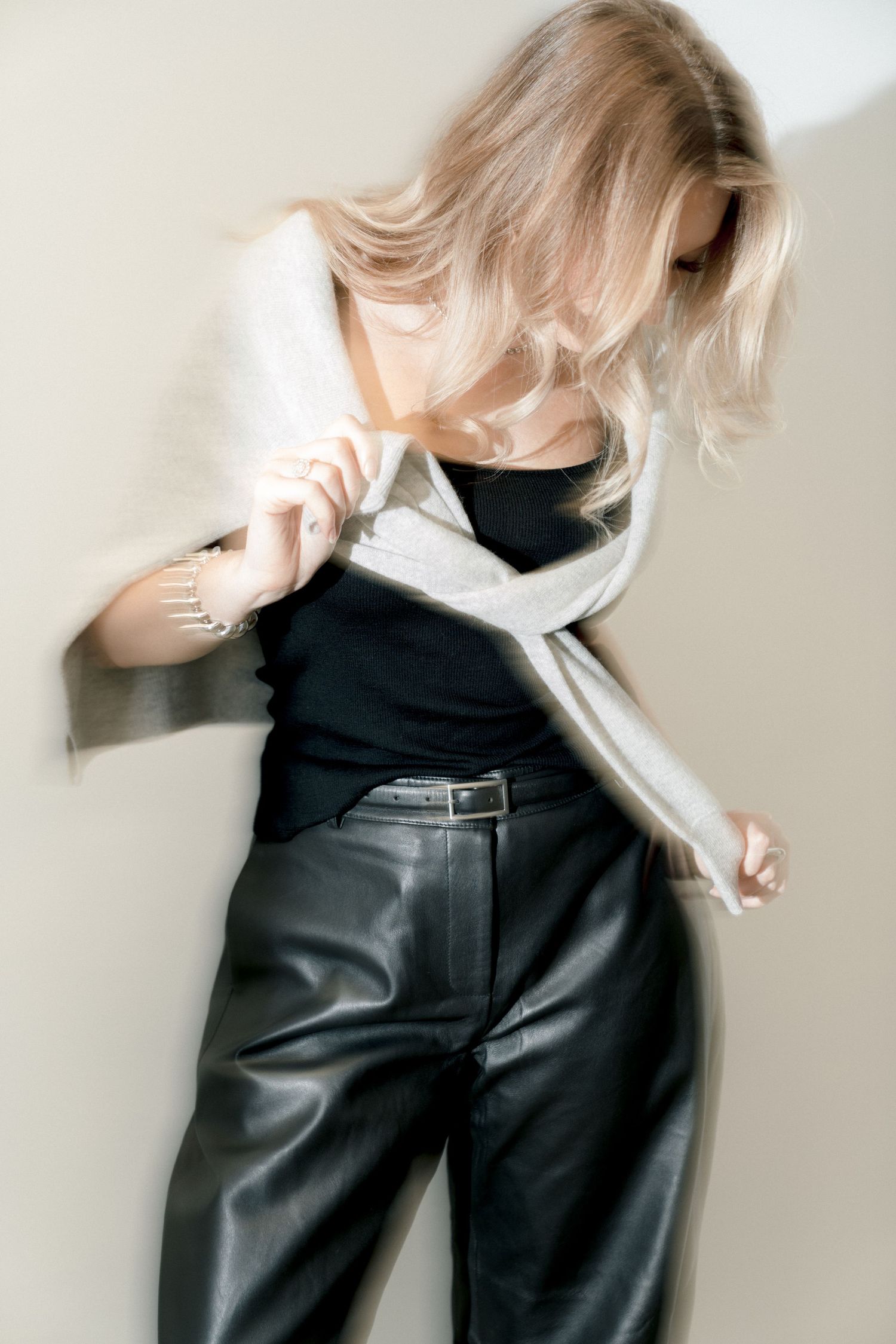 Dynamic fashion pose in black leather pants and contrasting light sweater with movement-focused styling.