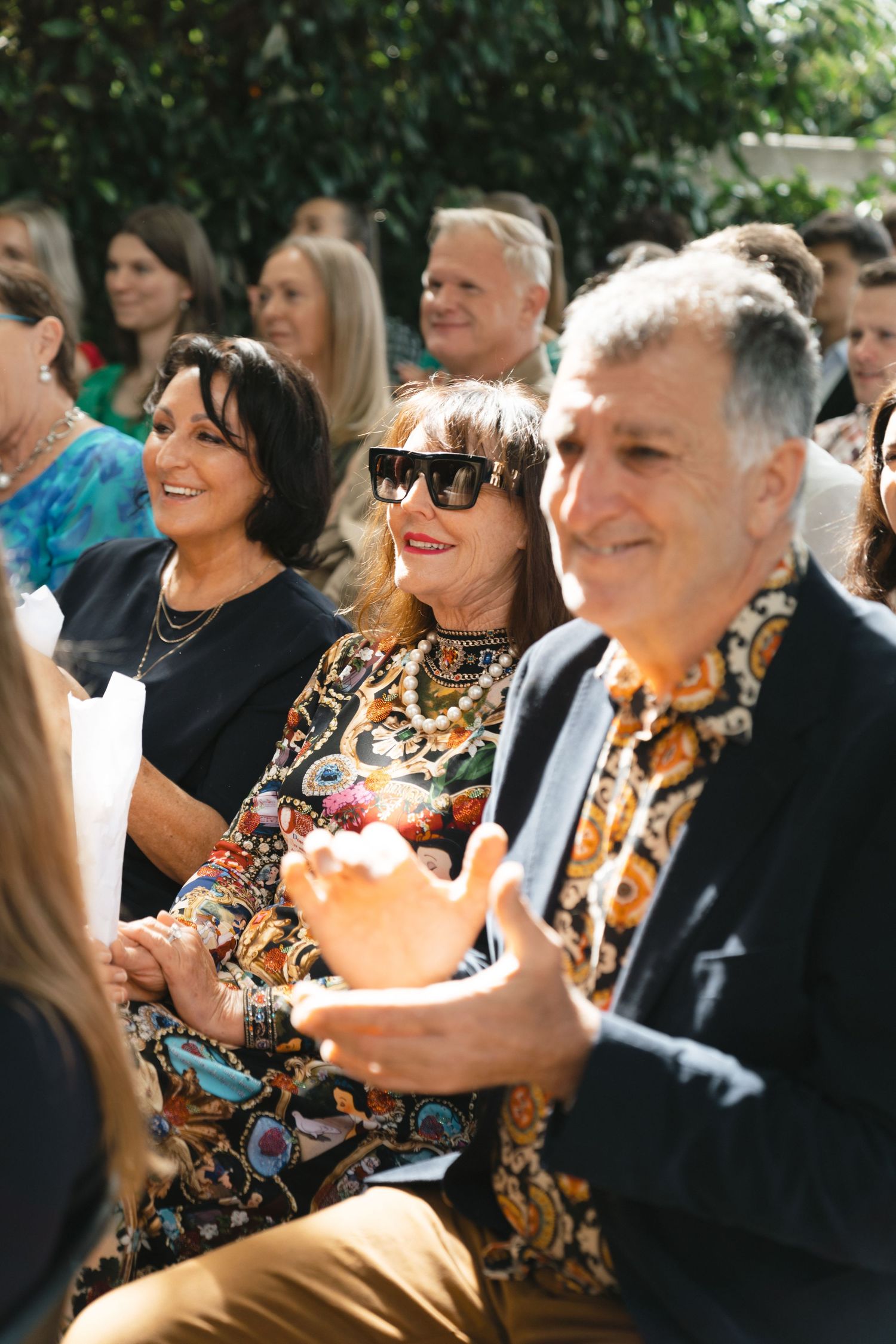 Wedding guests in colorful attire smile and enjoy the outdoor ceremony.