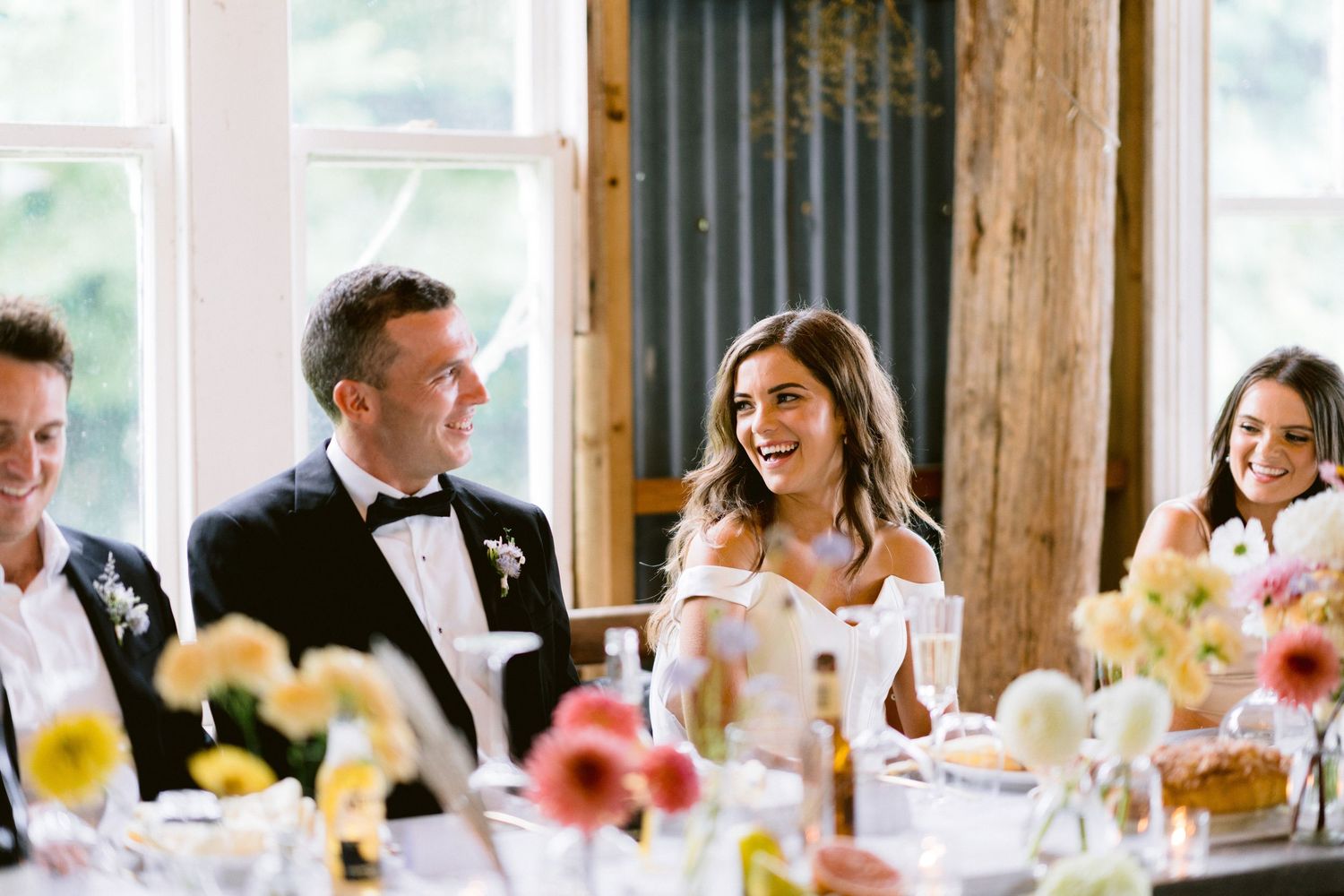 Rustic wedding reception dining area with wooden beams and large windows.