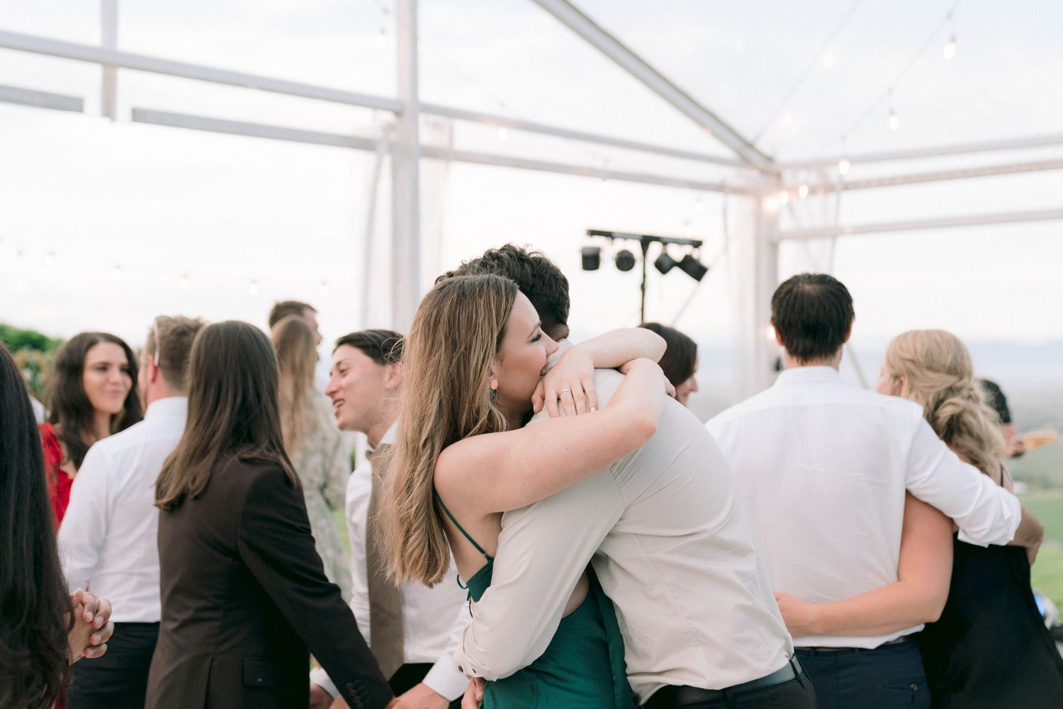 Wedding guests mingle under a white tent canopy during an outdoor reception.