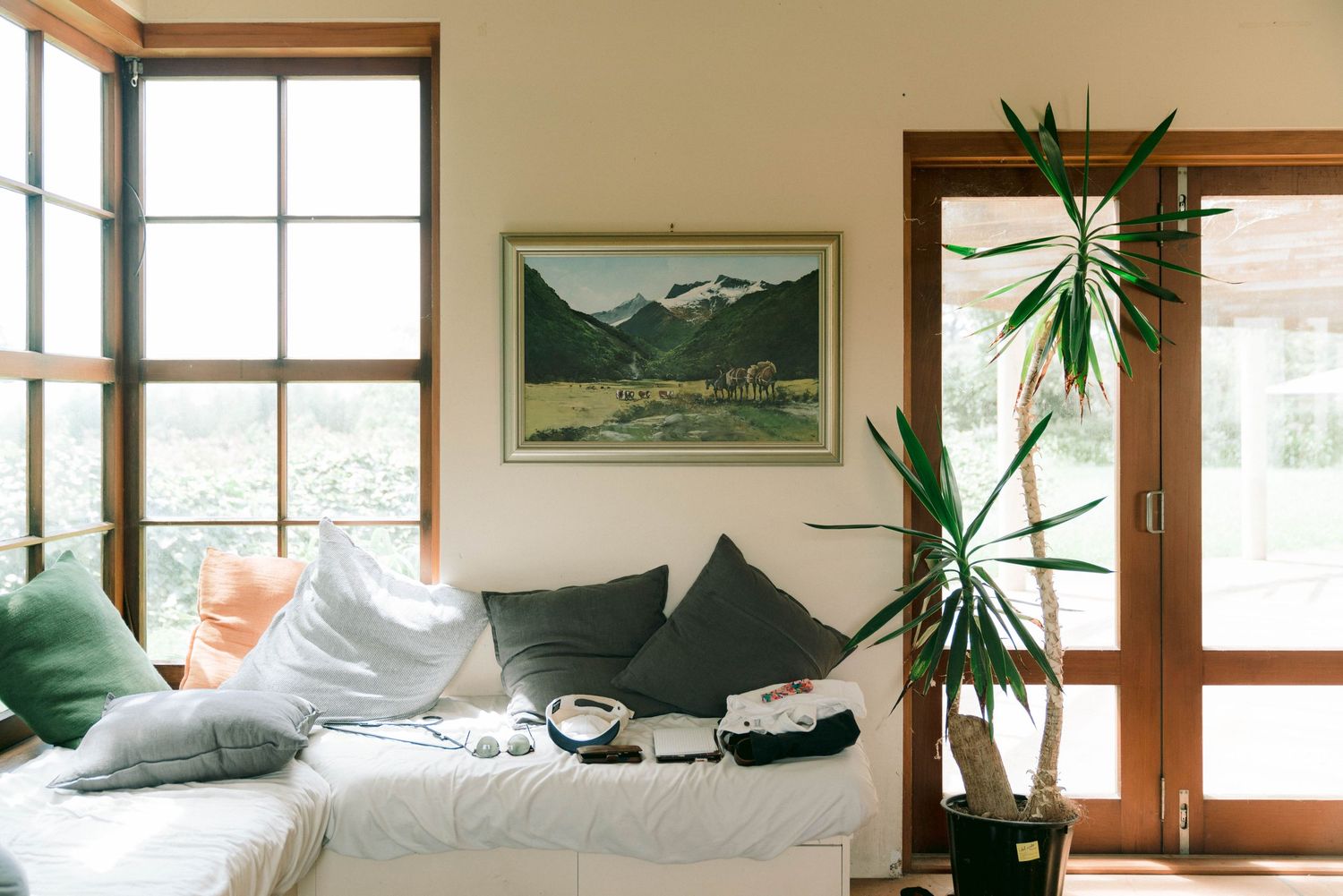 Cozy living room corner with landscape art, houseplant, and comfortable seating arrangement near windows.