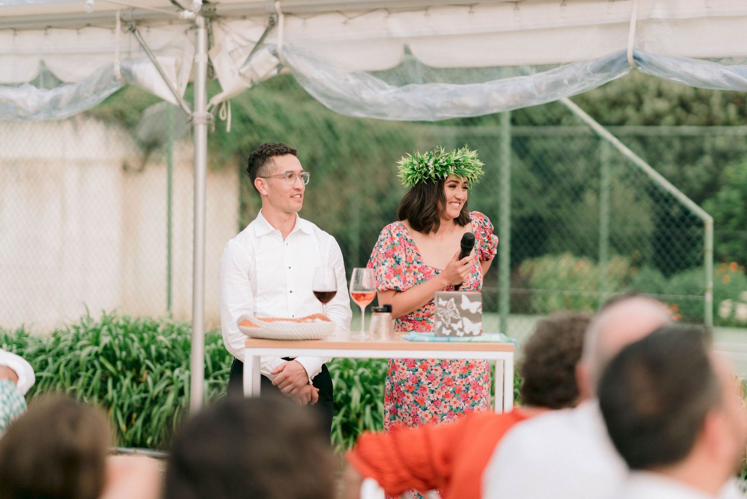 Wedding reception setup under white tent with greenery and table settings.