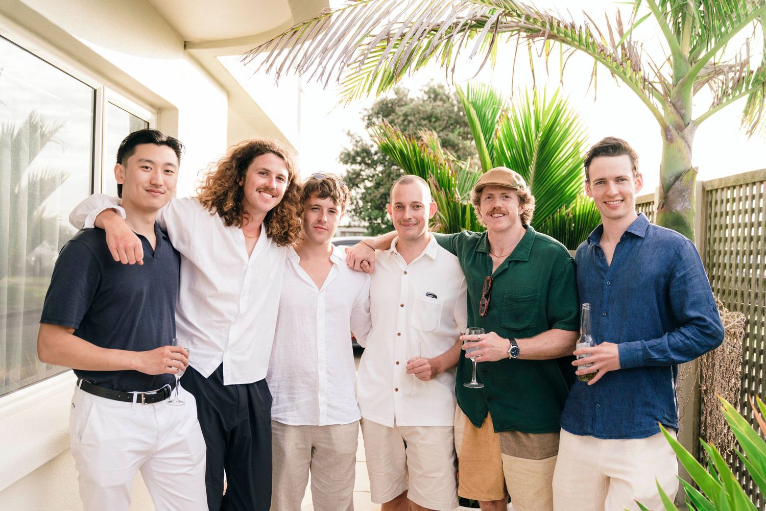 A group of well-dressed guests pose together on a palm tree-lined patio.