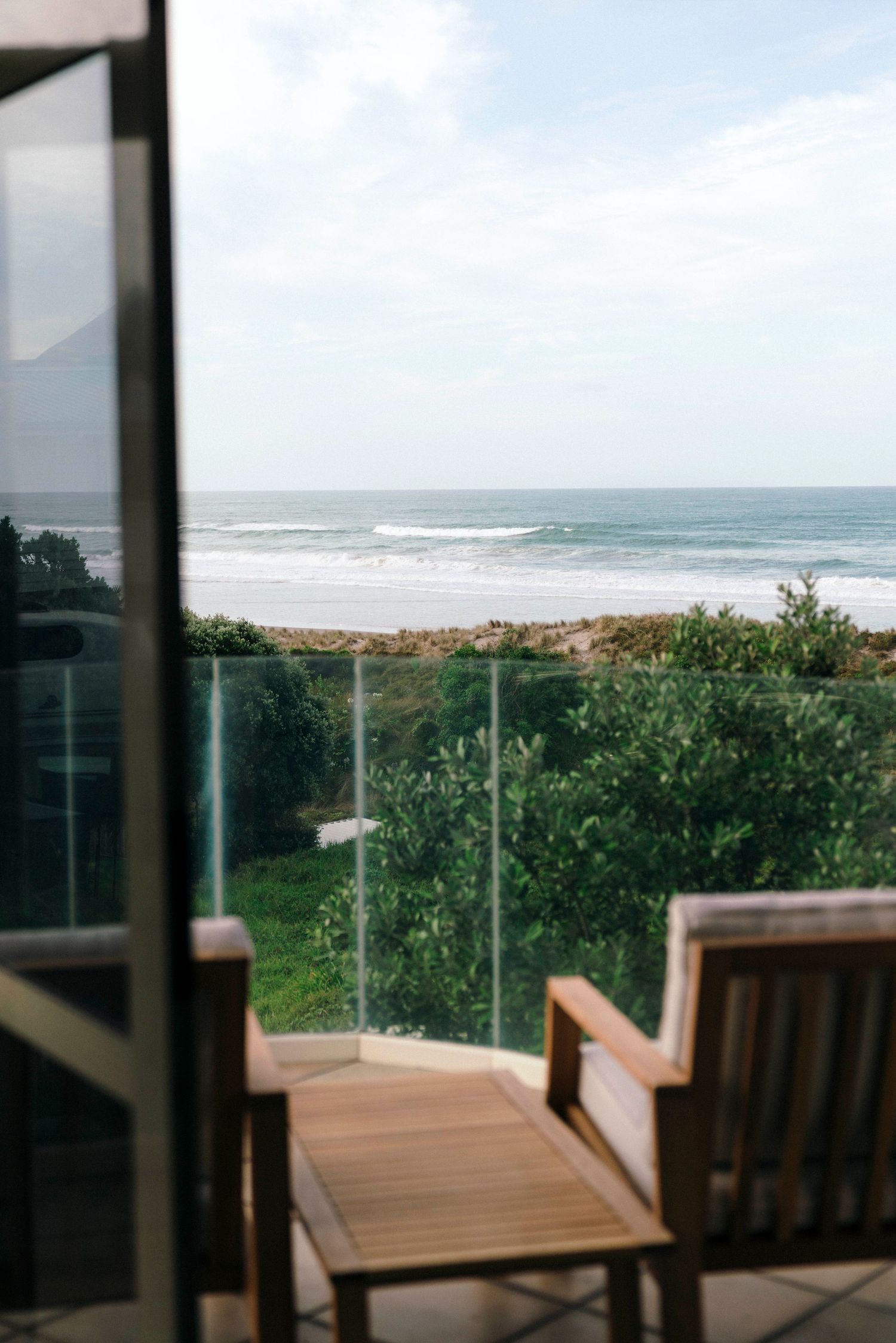 Wooden deck chair overlooking ocean waves through glass balcony railing.