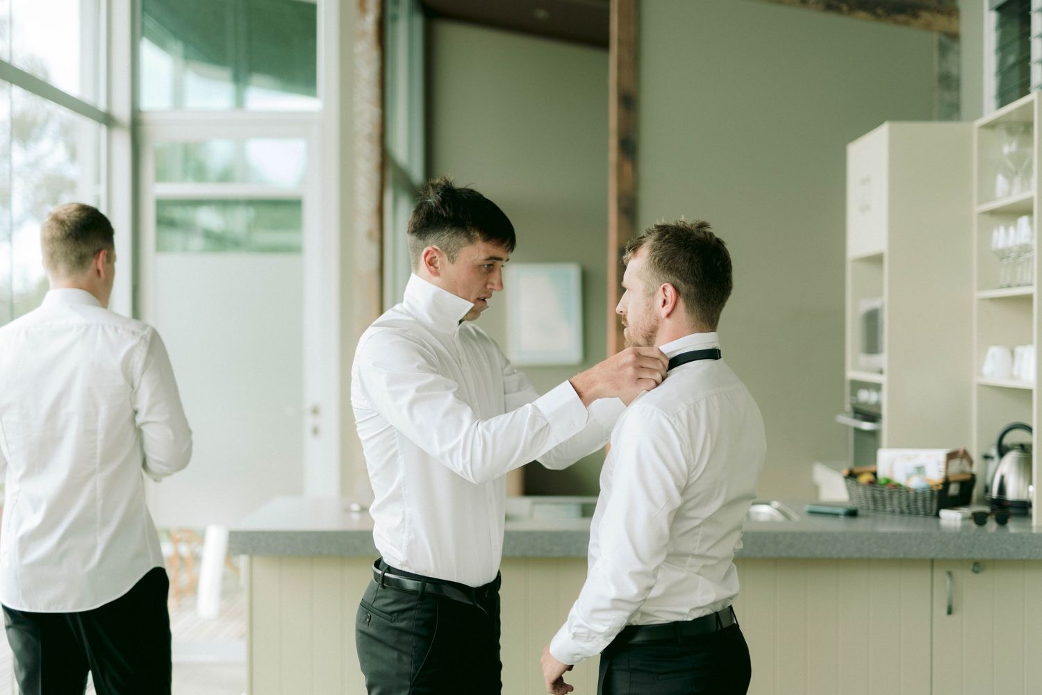 People in white dress shirts helping each other prepare for a formal event.