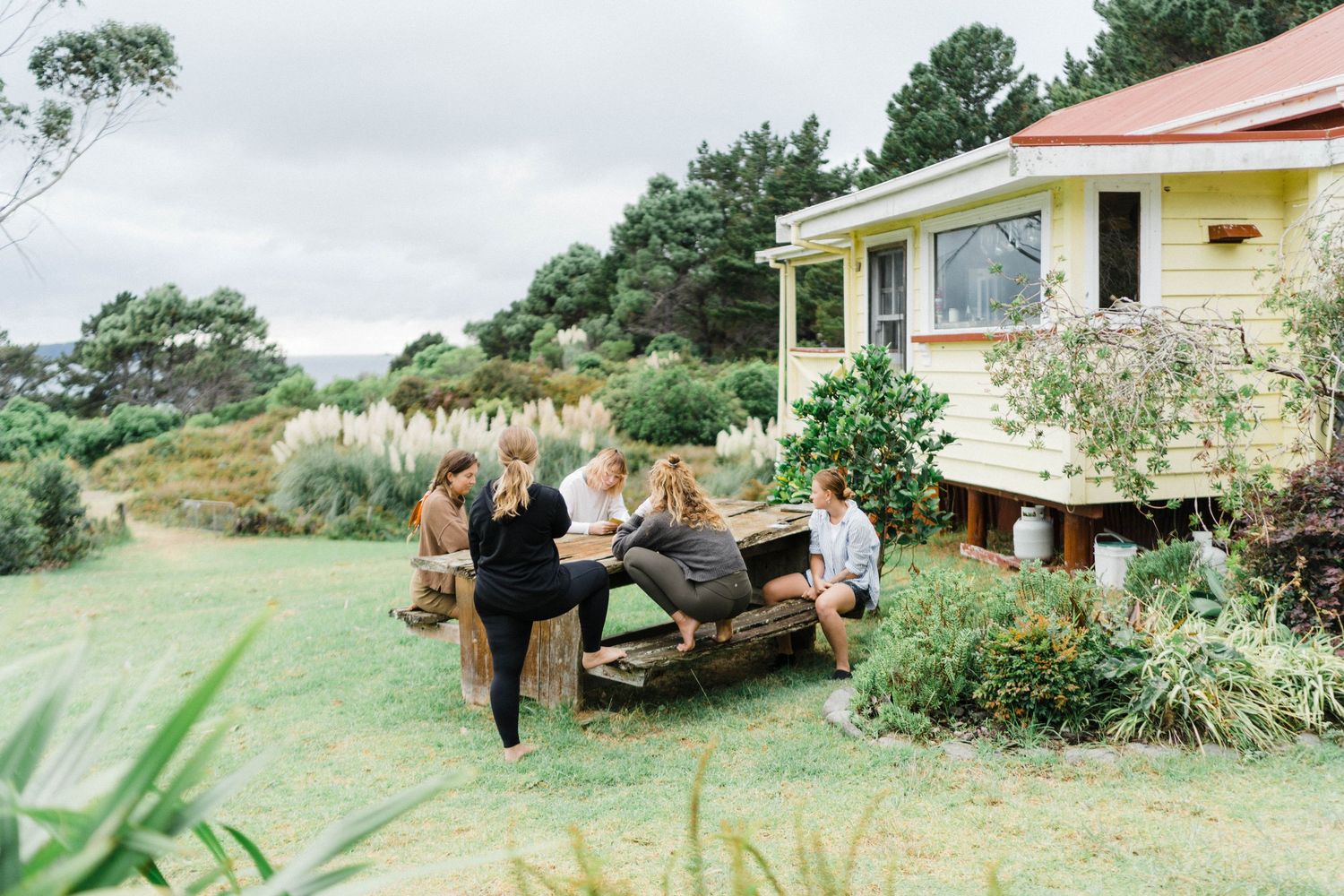 Group gathered for outdoor dining at a rustic countryside house with mountain views and lush gardens.