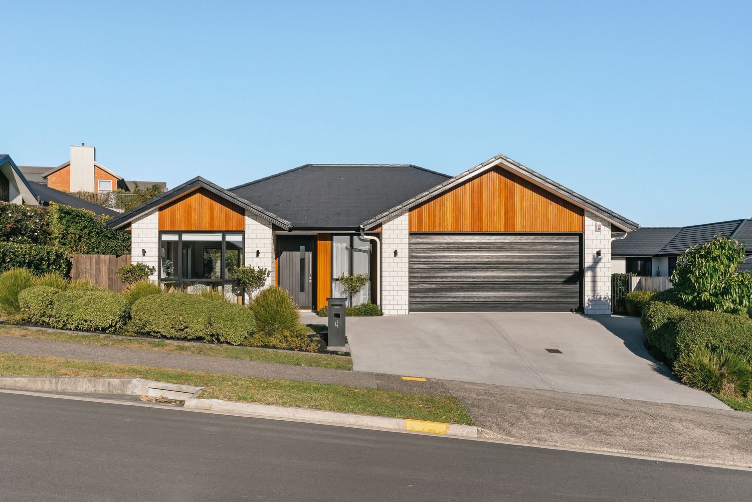 Modern single-story house exterior with dark roof and wooden accents viewed from the street.