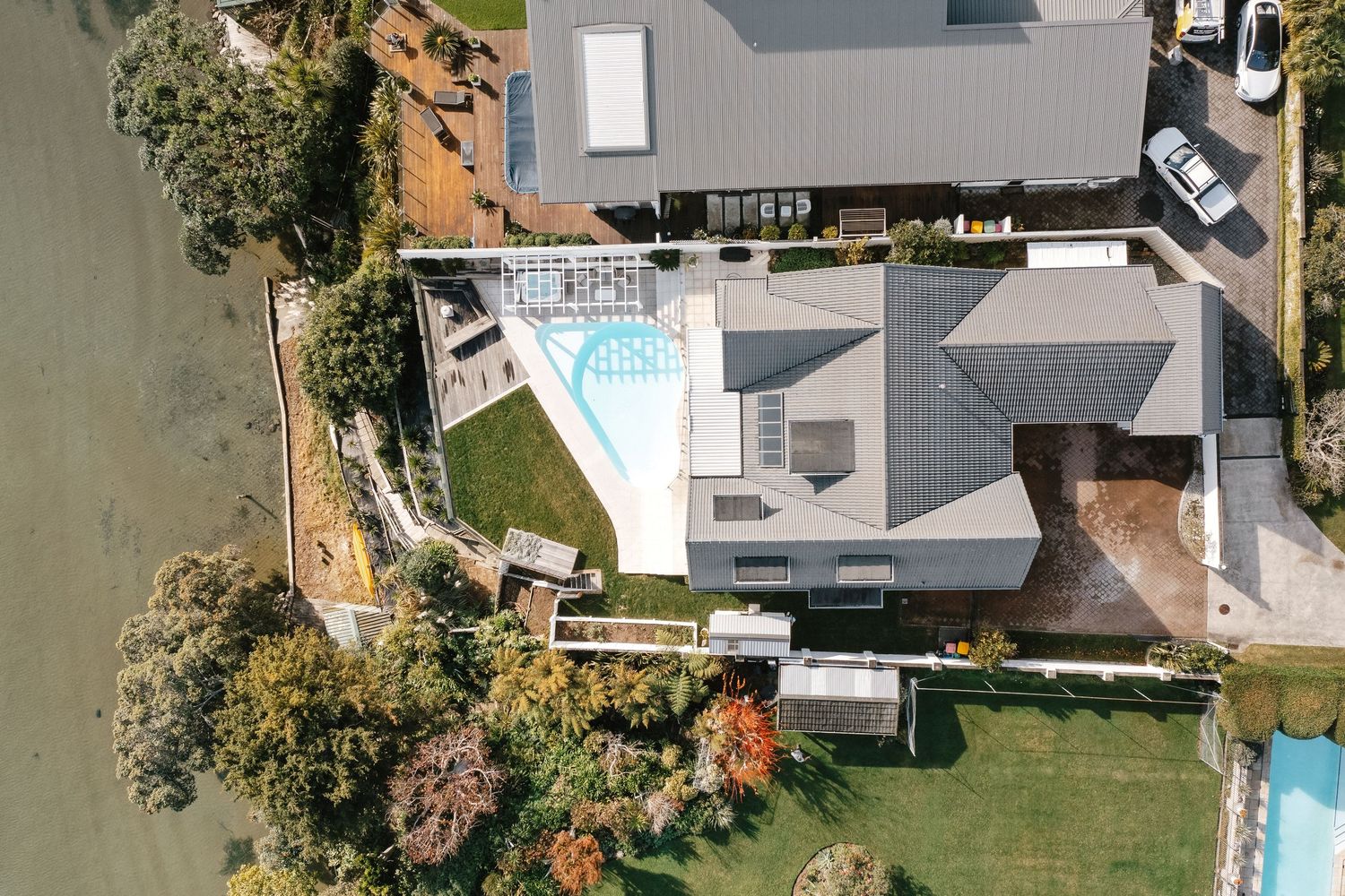 Aerial view of modern waterfront home with pool and landscaped yard.