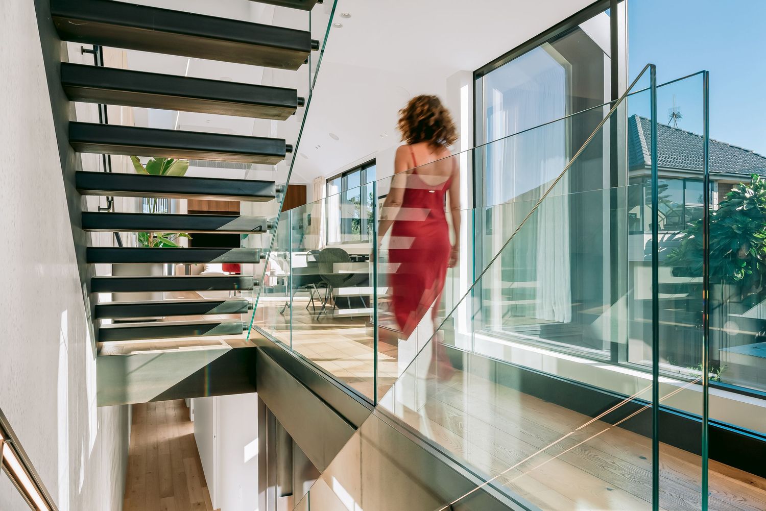 Contemporary floating staircase with glass panels and black metal frame in a modern house.