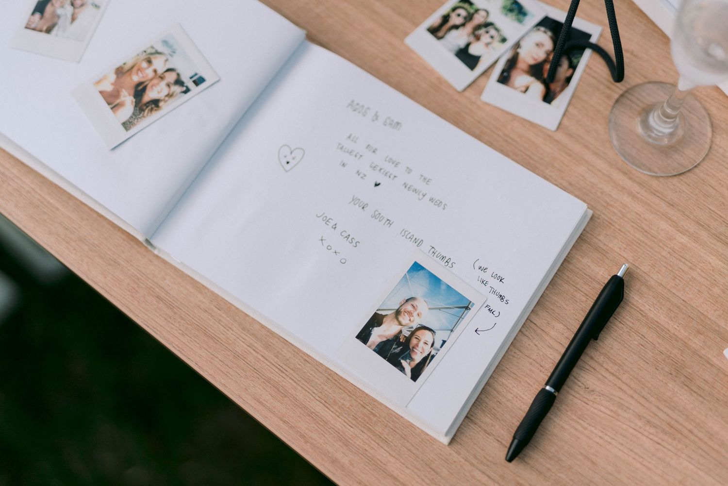 A wedding photo album and guest book laid out on a wooden table with a pen for signing.