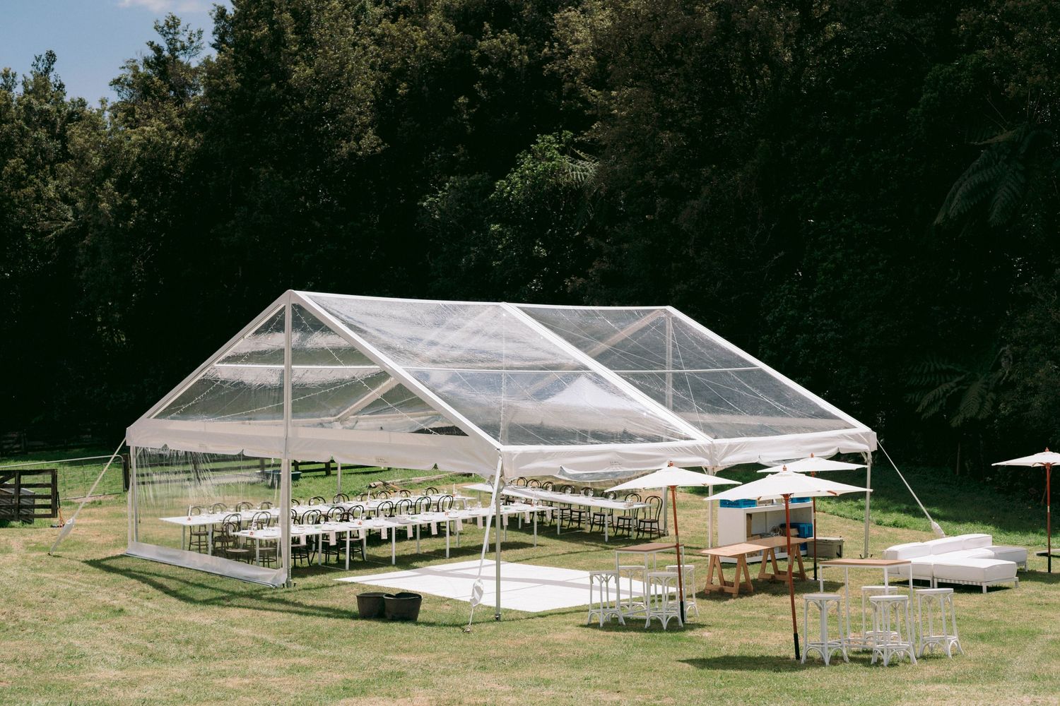 Clear tent structure set up for outdoor wedding reception with white chairs arranged in rows.