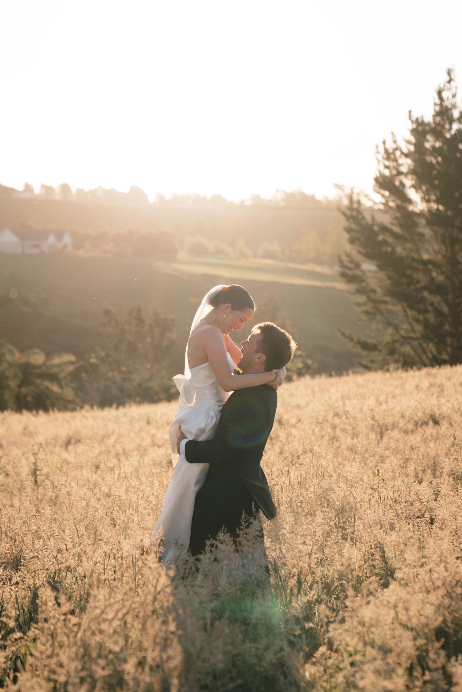 A couple embraces in a sun-drenched field during golden hour on their wedding day.