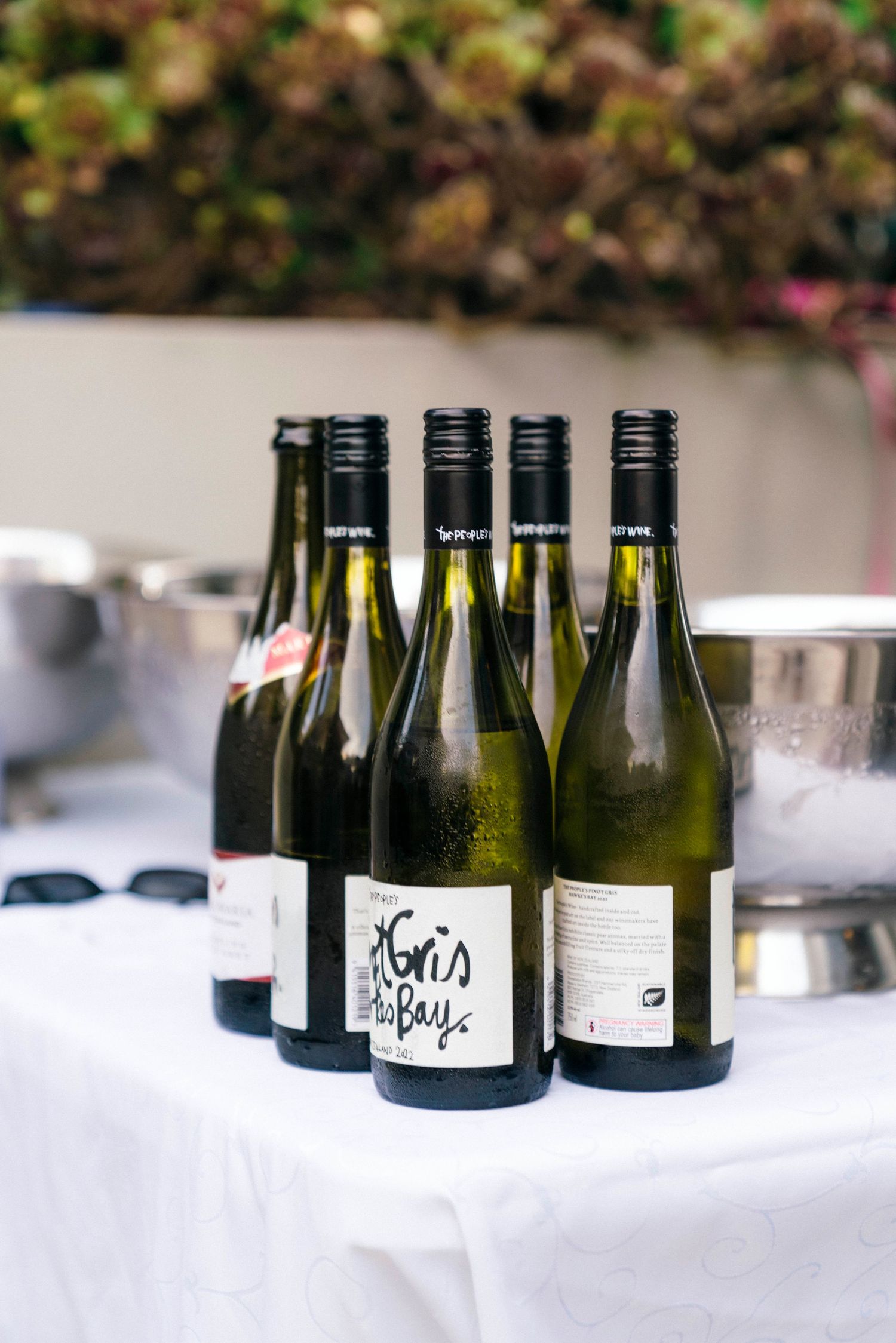 Dark wine bottles lined up on a white tablecloth at what appears to be a catering or event setup.