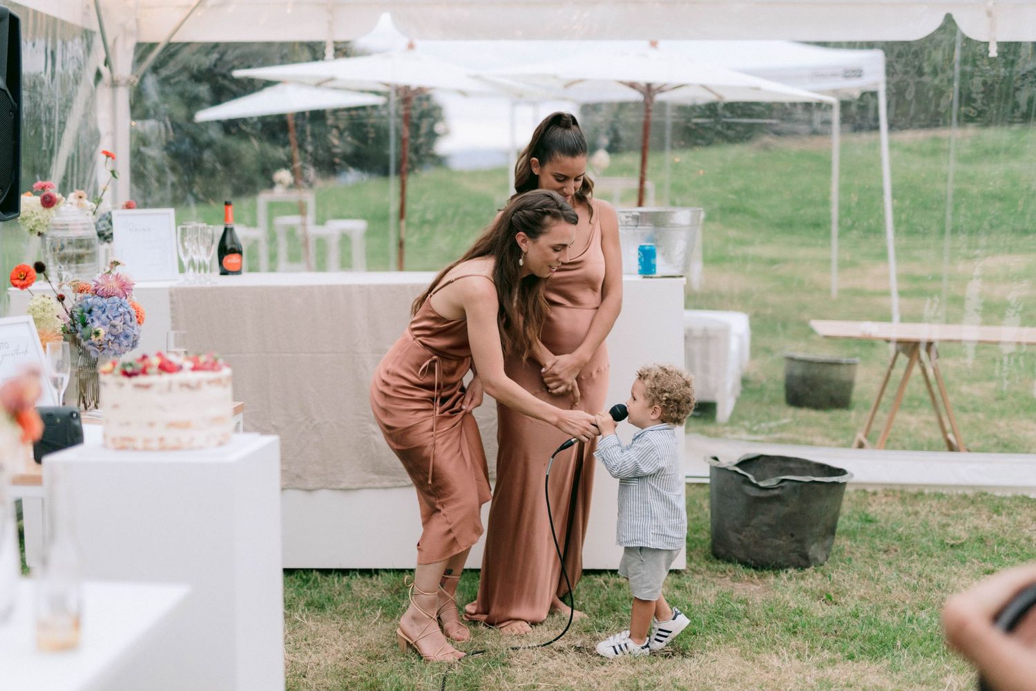 Wedding guests in dusty rose dresses share a playful moment at an outdoor reception.