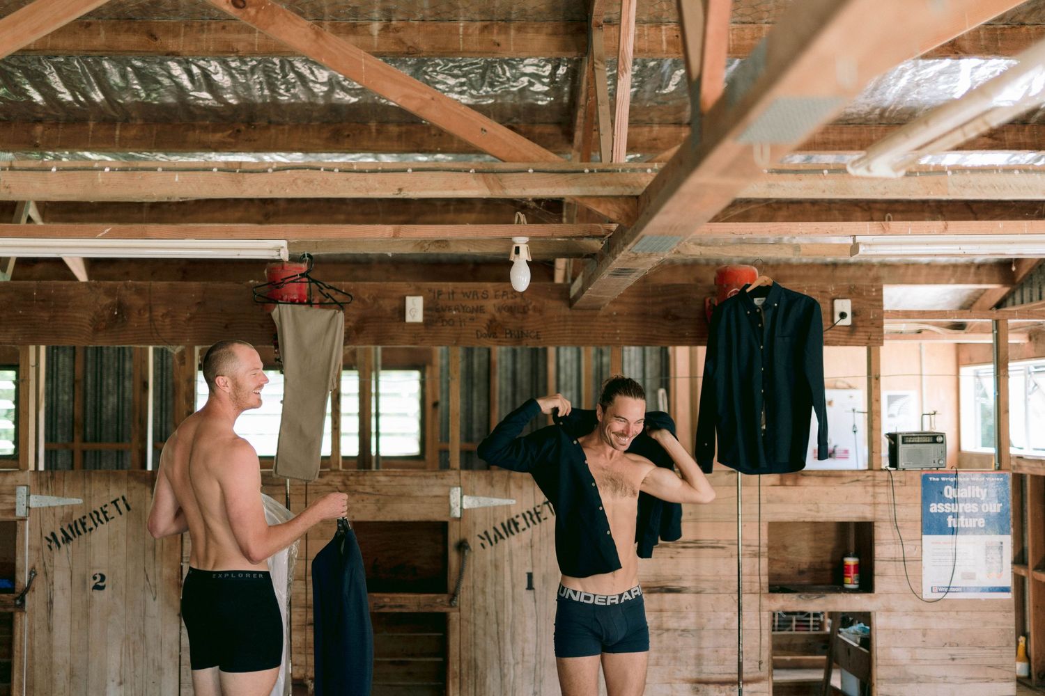 Rustic wooden interior of a barn venue with exposed beams and hanging clothing.
