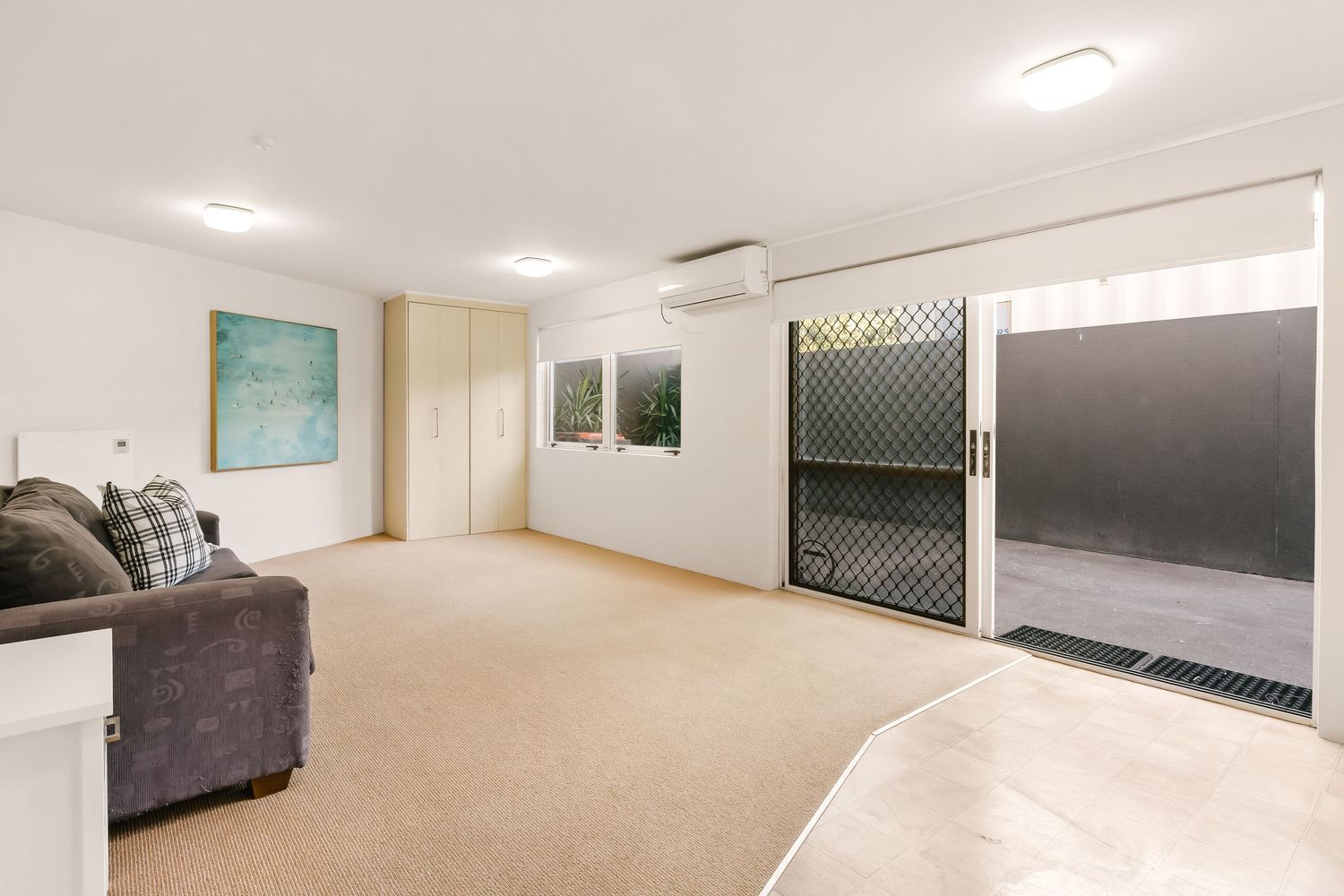 Modern basement living space with carpeted floors, grey couch and sliding glass doors leading outside.