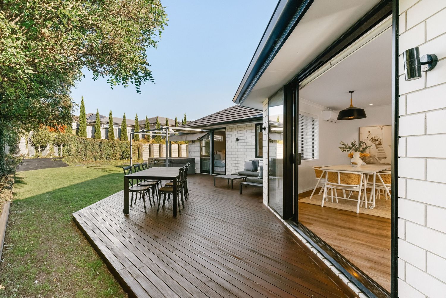 Modern home exterior featuring a spacious wooden deck with outdoor dining furniture and sliding glass doors leading inside.
