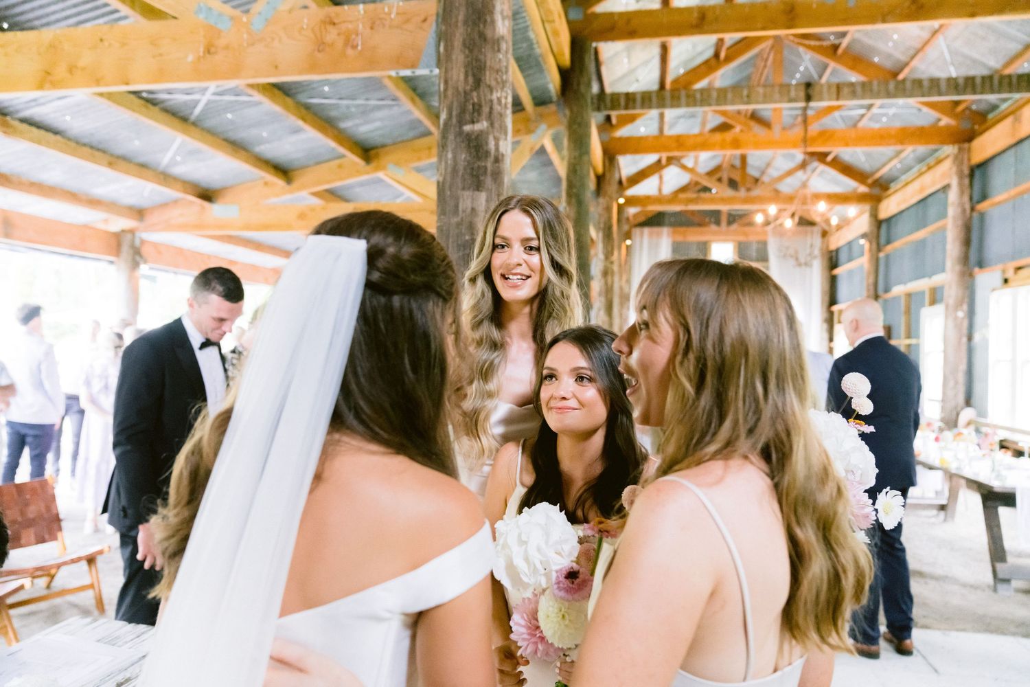 Wedding reception in a rustic barn venue with exposed wooden beams and white draping.