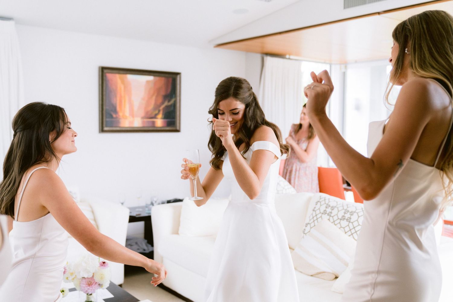 Group of women in white dresses preparing for a wedding celebration in a bright indoor space.