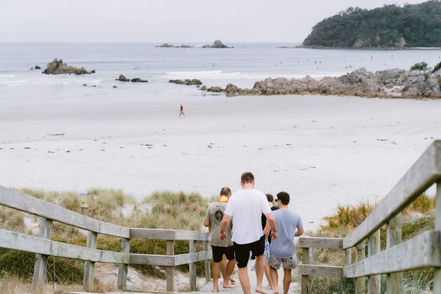 A wooden walkway leads across sandy dunes to a scenic ocean beach on a calm summer day.